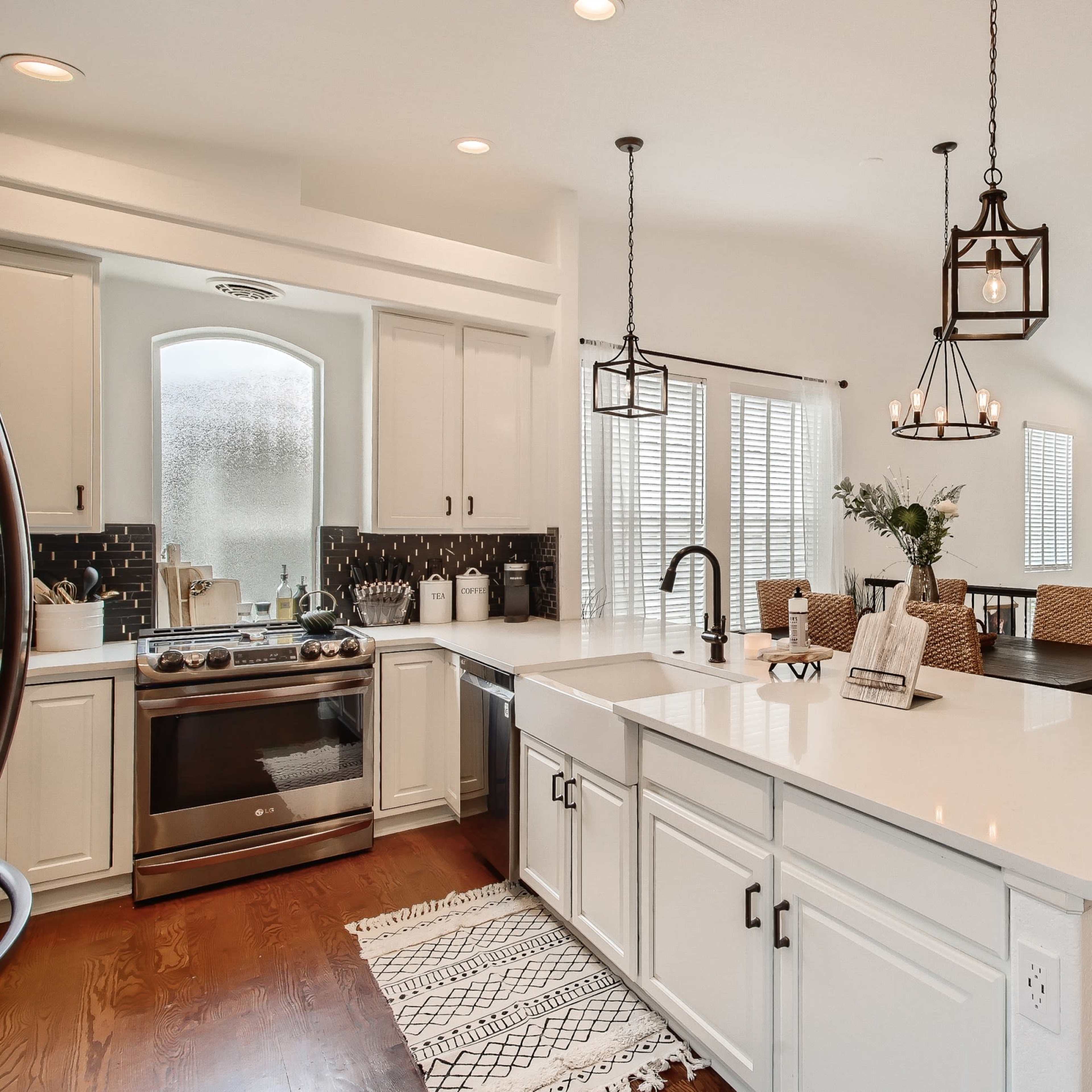 A modern kitchen features a central island with a sink, surrounded by white cabinetry, and is connected to a dining area illuminated by pendant lights.