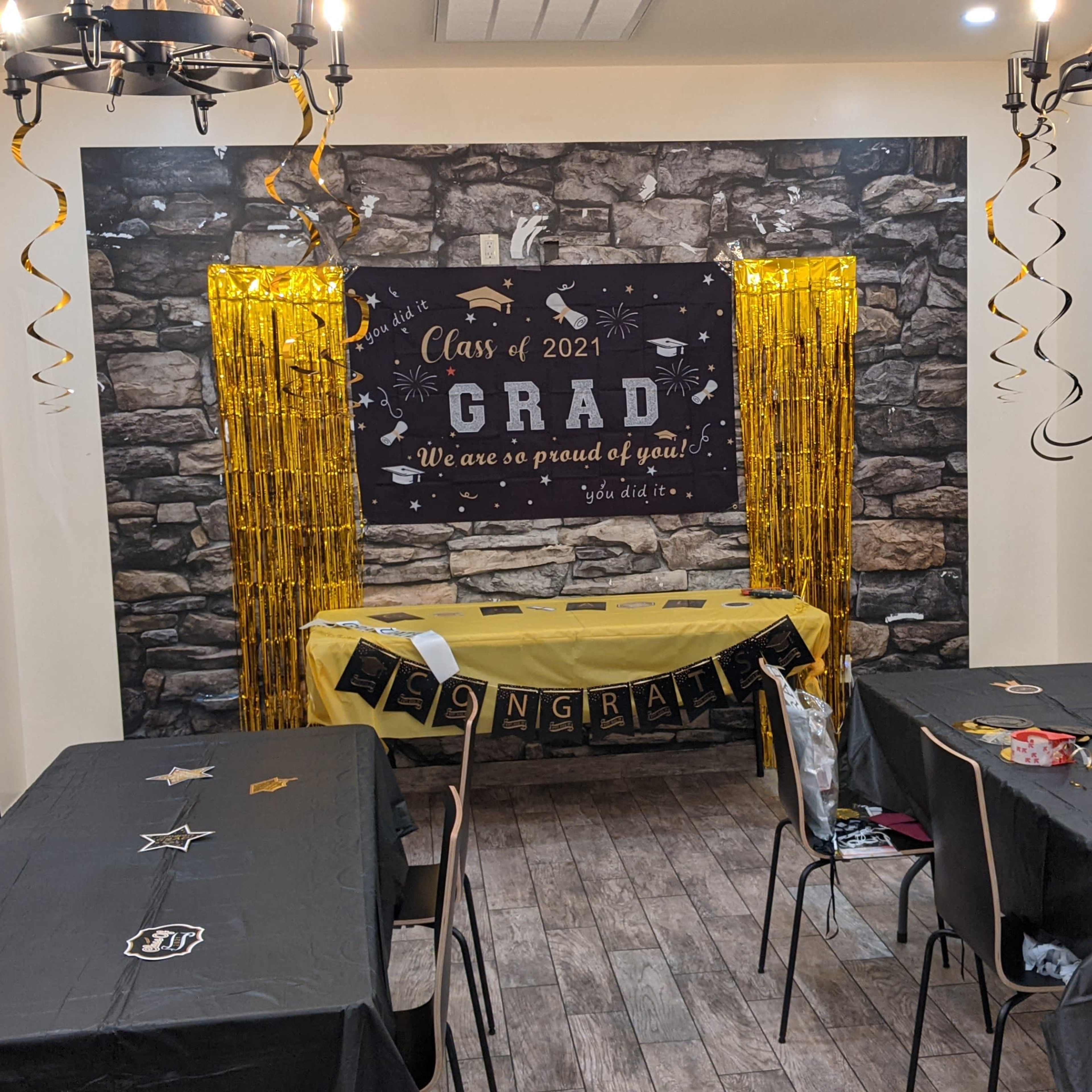 A decorated room for a graduation celebration, featuring a black and yellow theme with tables, a festive banner, and wall decorations.