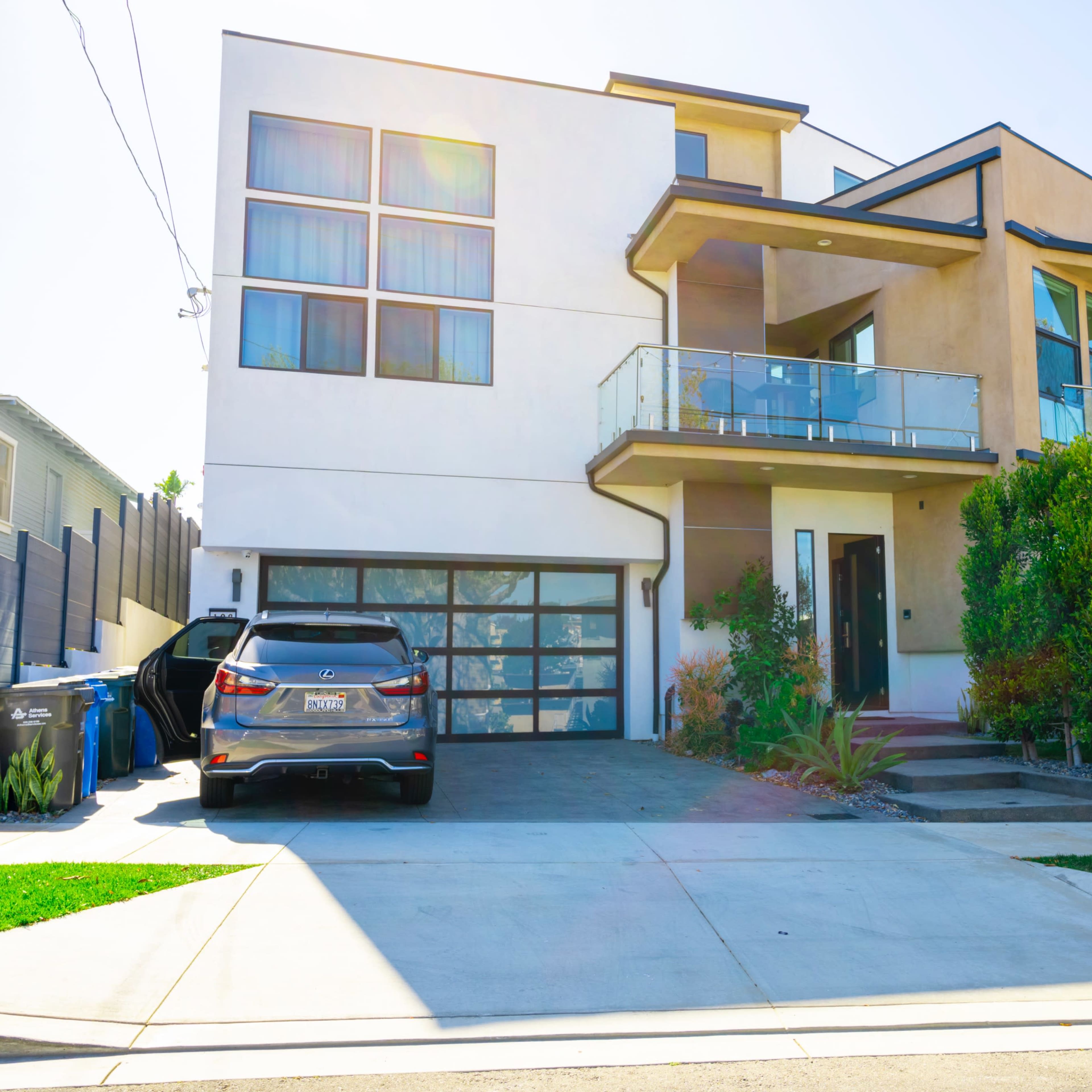 A modern two-story house with large windows, a balcony, and a driveway with a parked car.