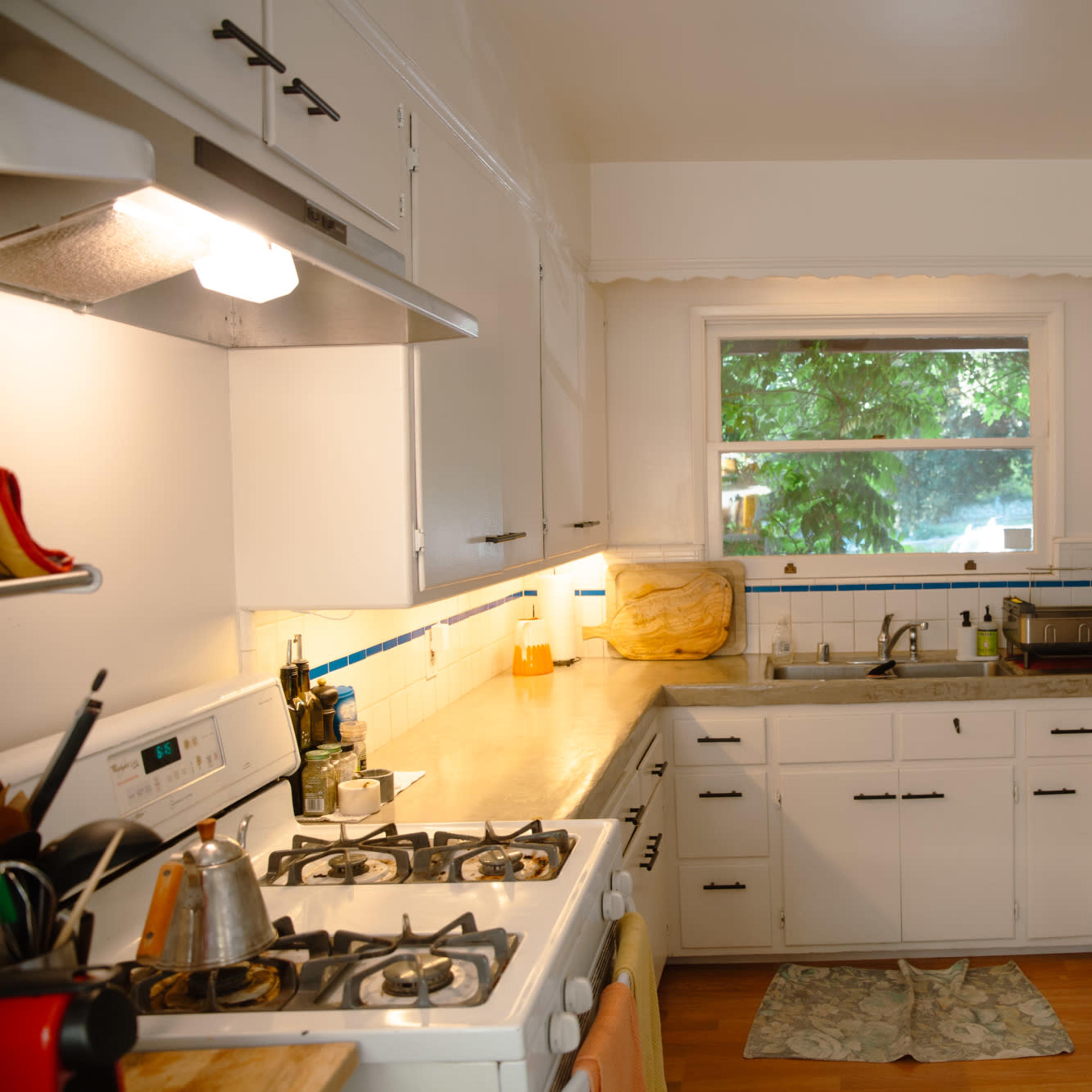 A bright kitchen features white cabinets, a gas stove, and a window overlooking greenery.