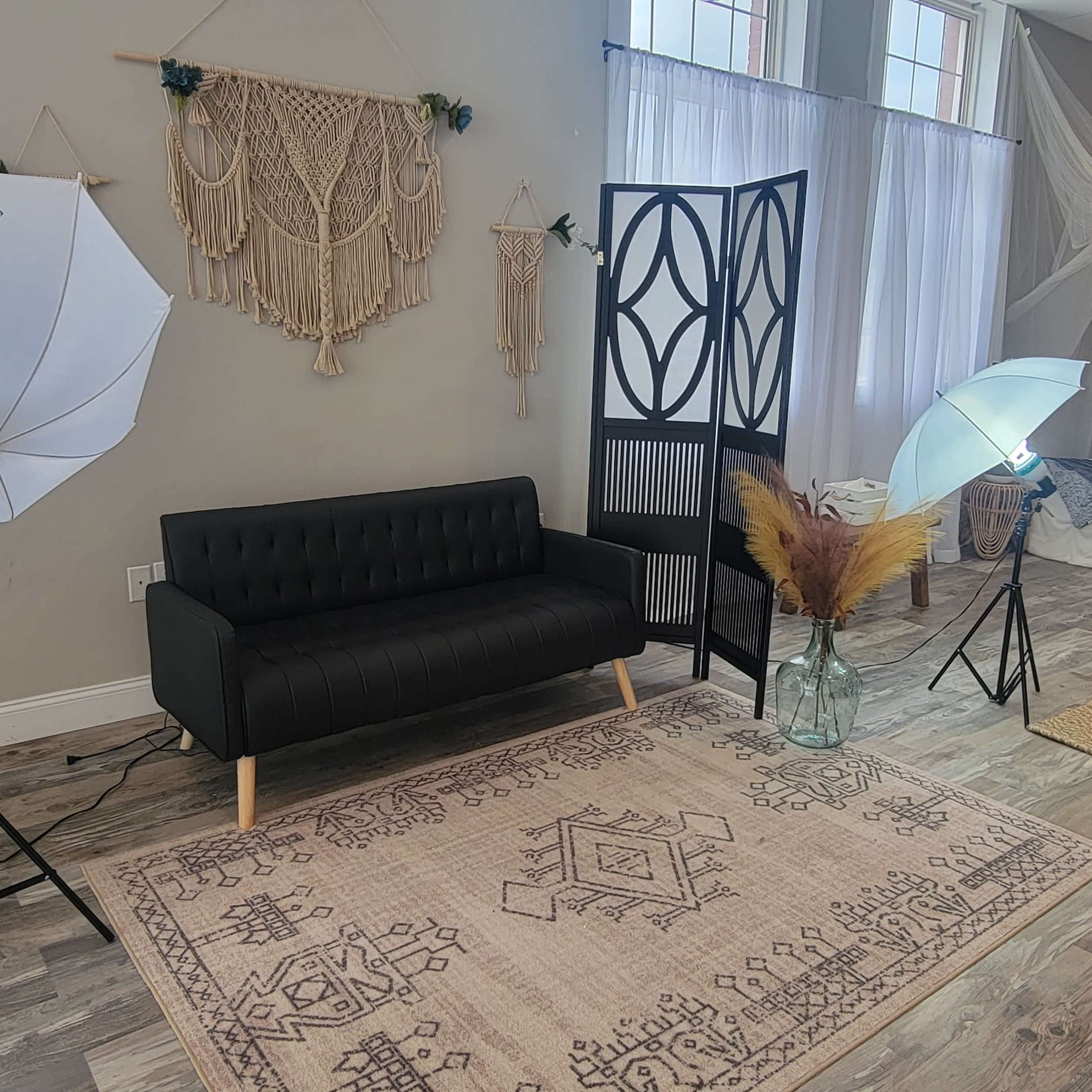 A photography studio with a black couch, two lighting umbrellas, a decorative backdrop, and a cozy seating area with a bed and various textiles.