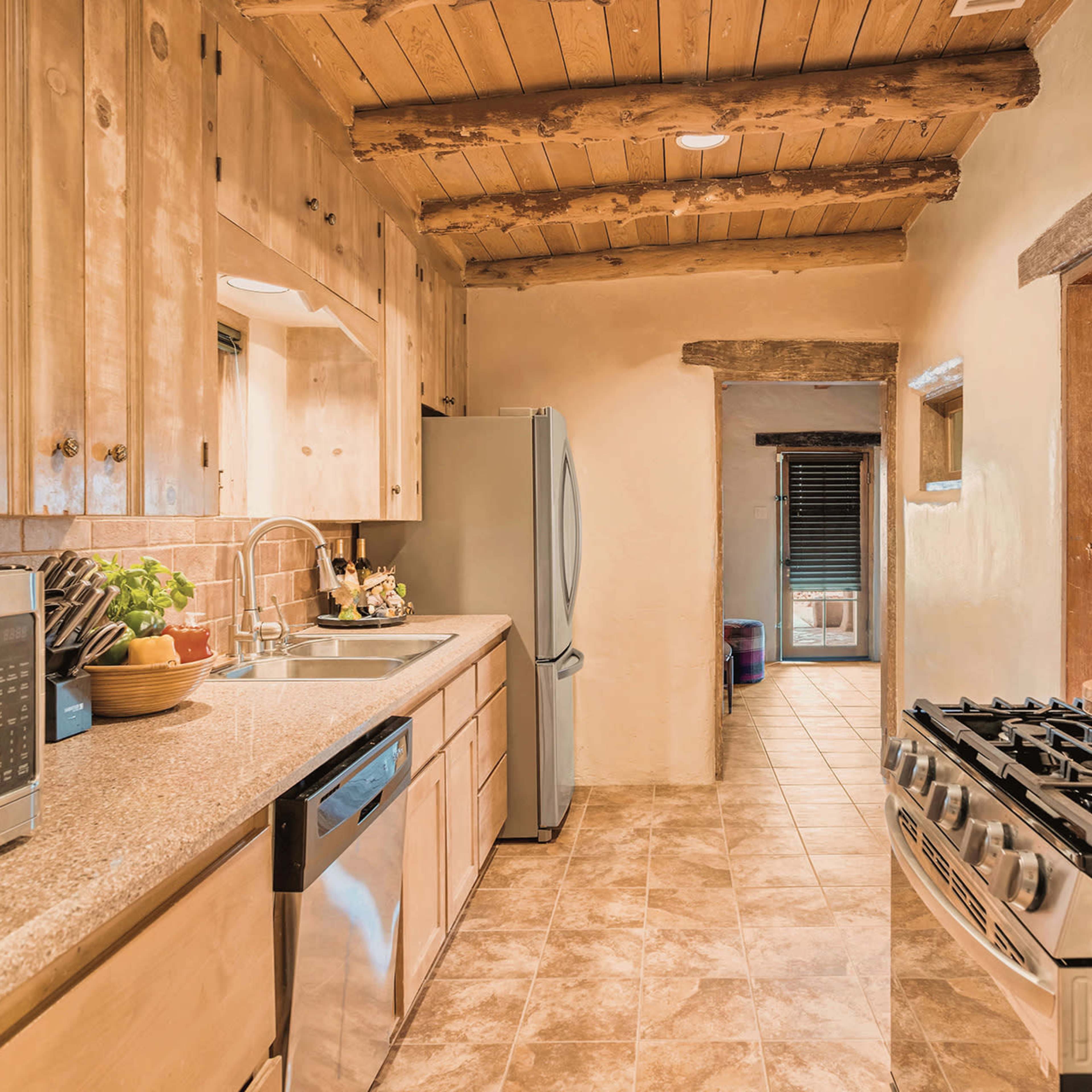 The kitchen features wooden cabinetry, stainless steel appliances, and a tile floor, with a view leading to a hallway.
