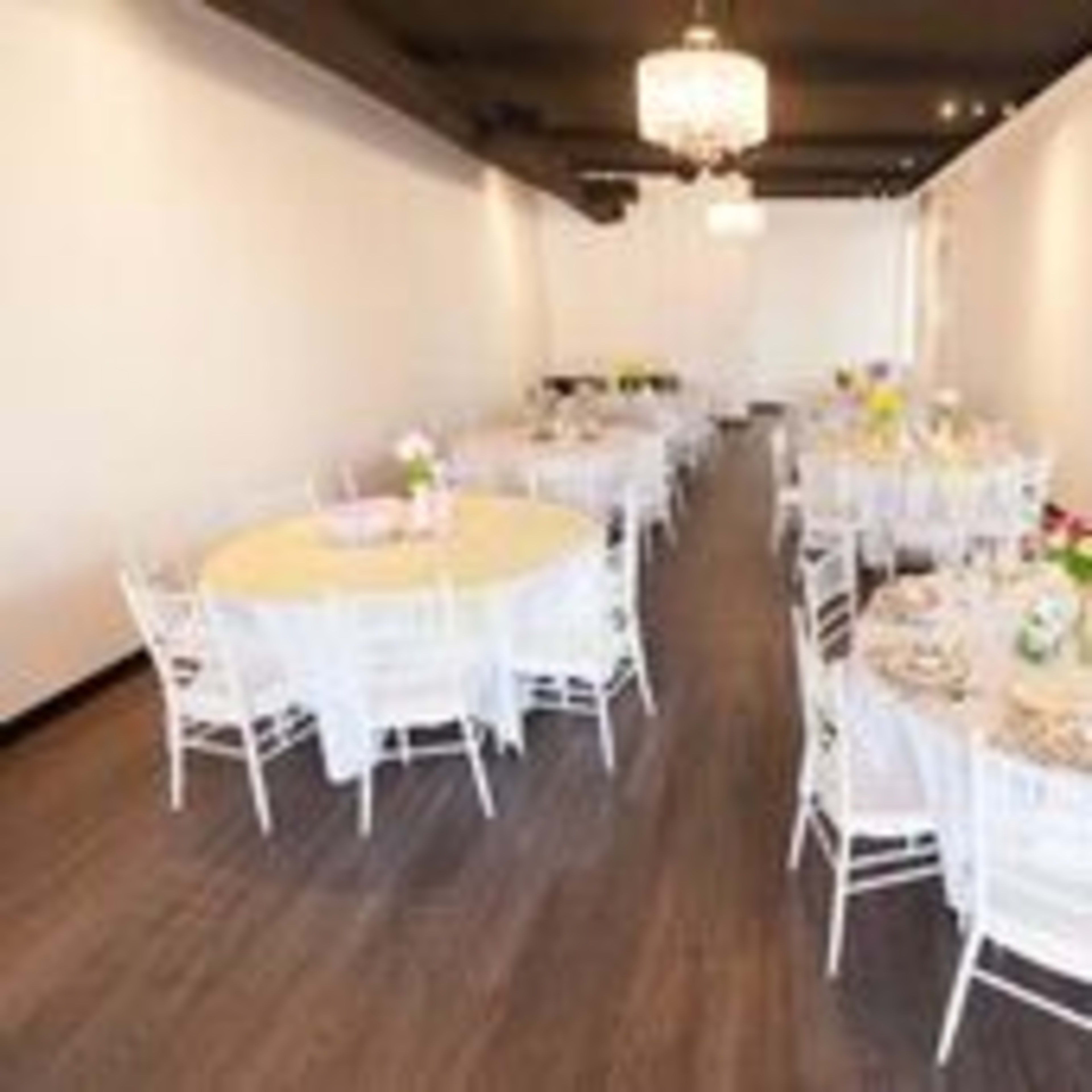 A spacious event room set with round tables covered in white tablecloths and adorned with floral centerpieces.