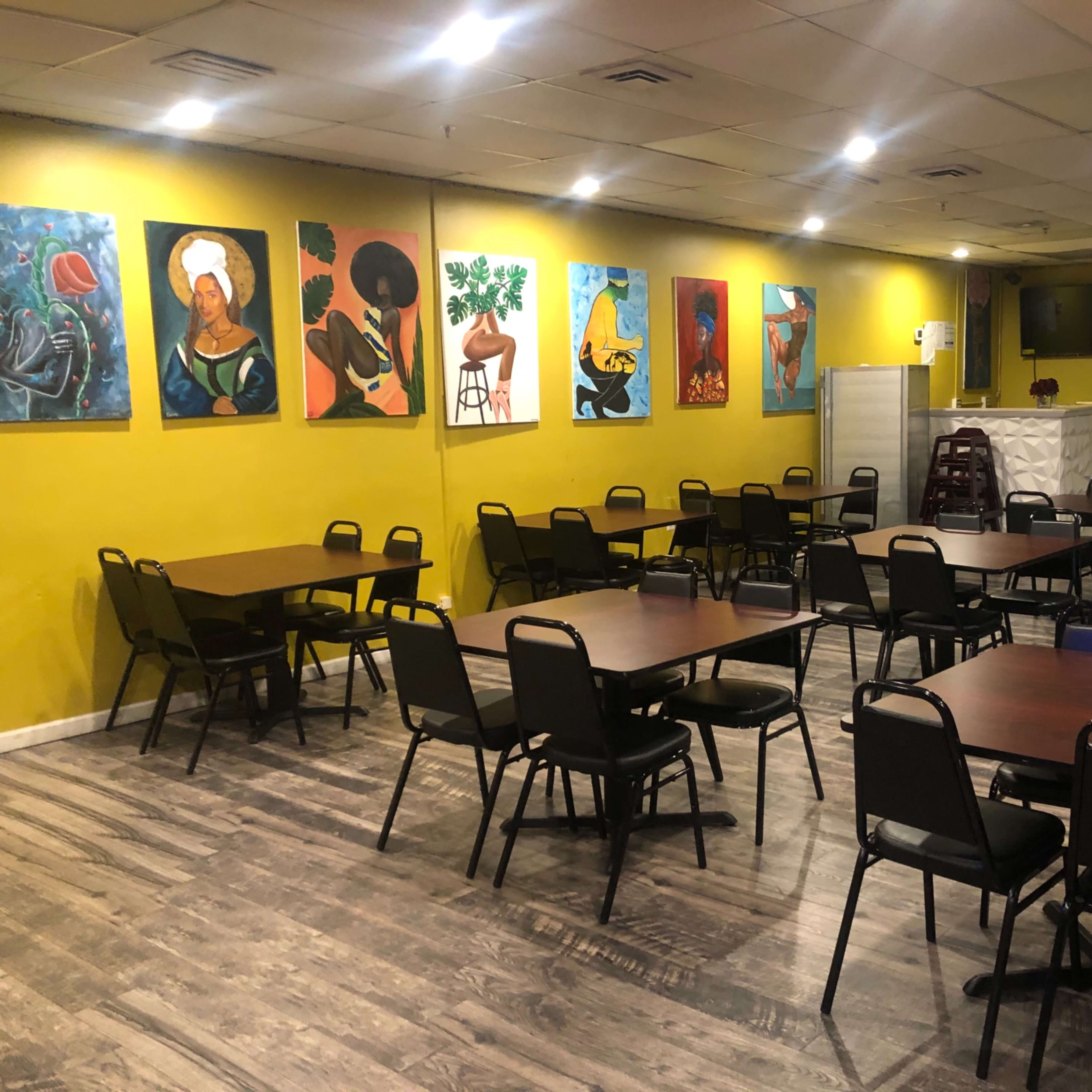 A brightly colored dining area with multiple empty tables and chairs arranged neatly, adorned with various paintings on the yellow walls.