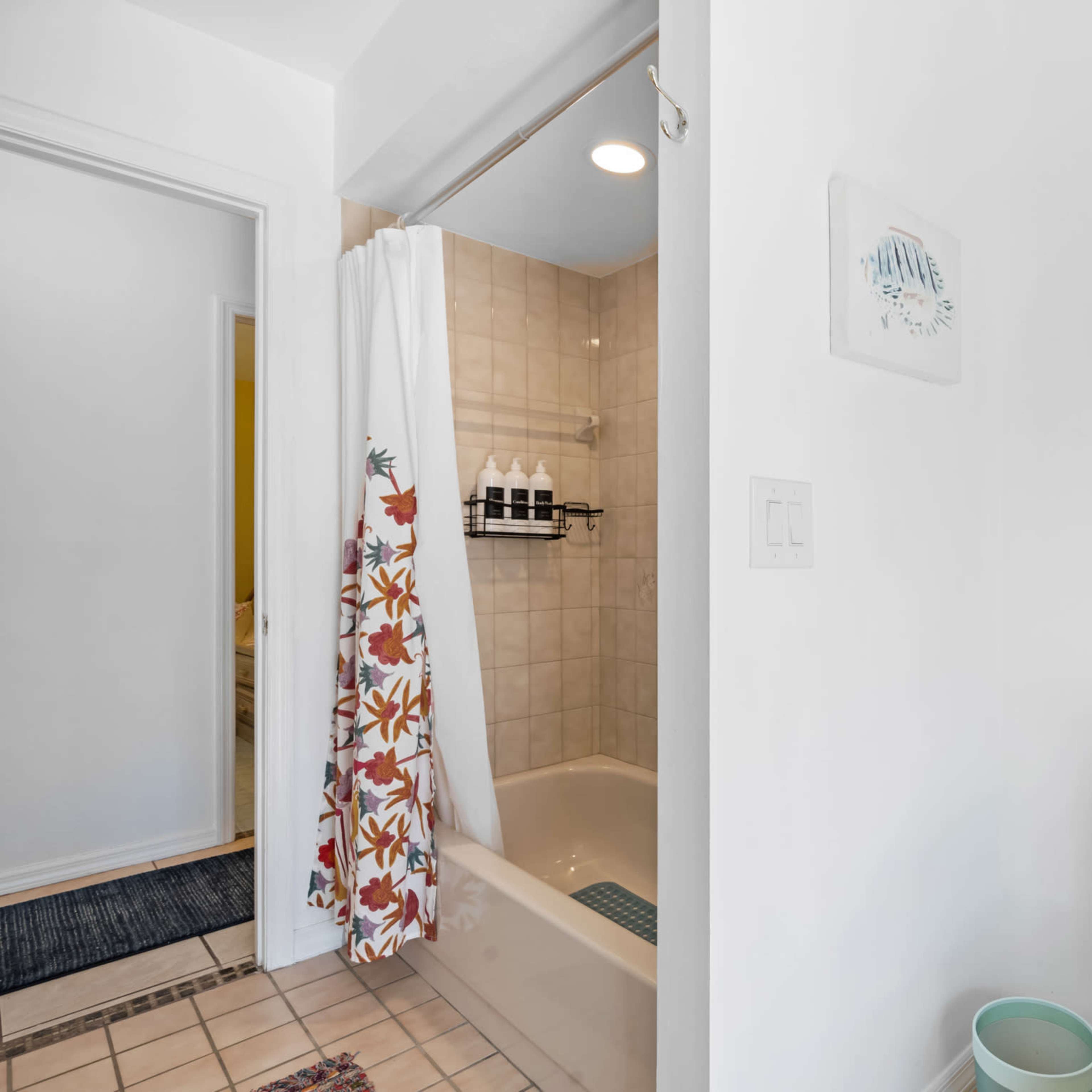 A bathroom with a toilet on the right, a shower area with a floral curtain in the back, and neatly arranged towels on the wall.