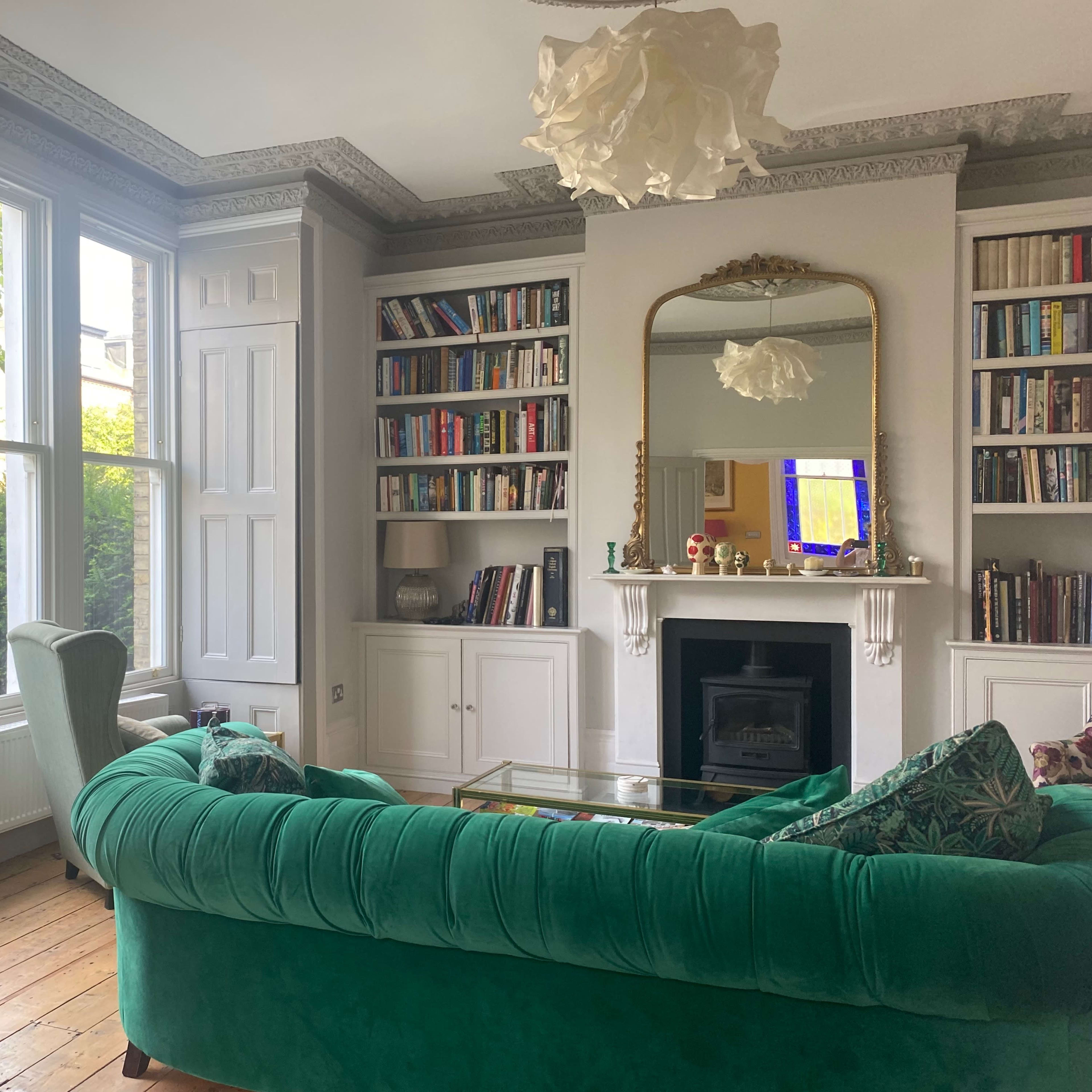 A living room with a green sofa, bookshelves filled with books, a fireplace, and large windows allowing natural light.