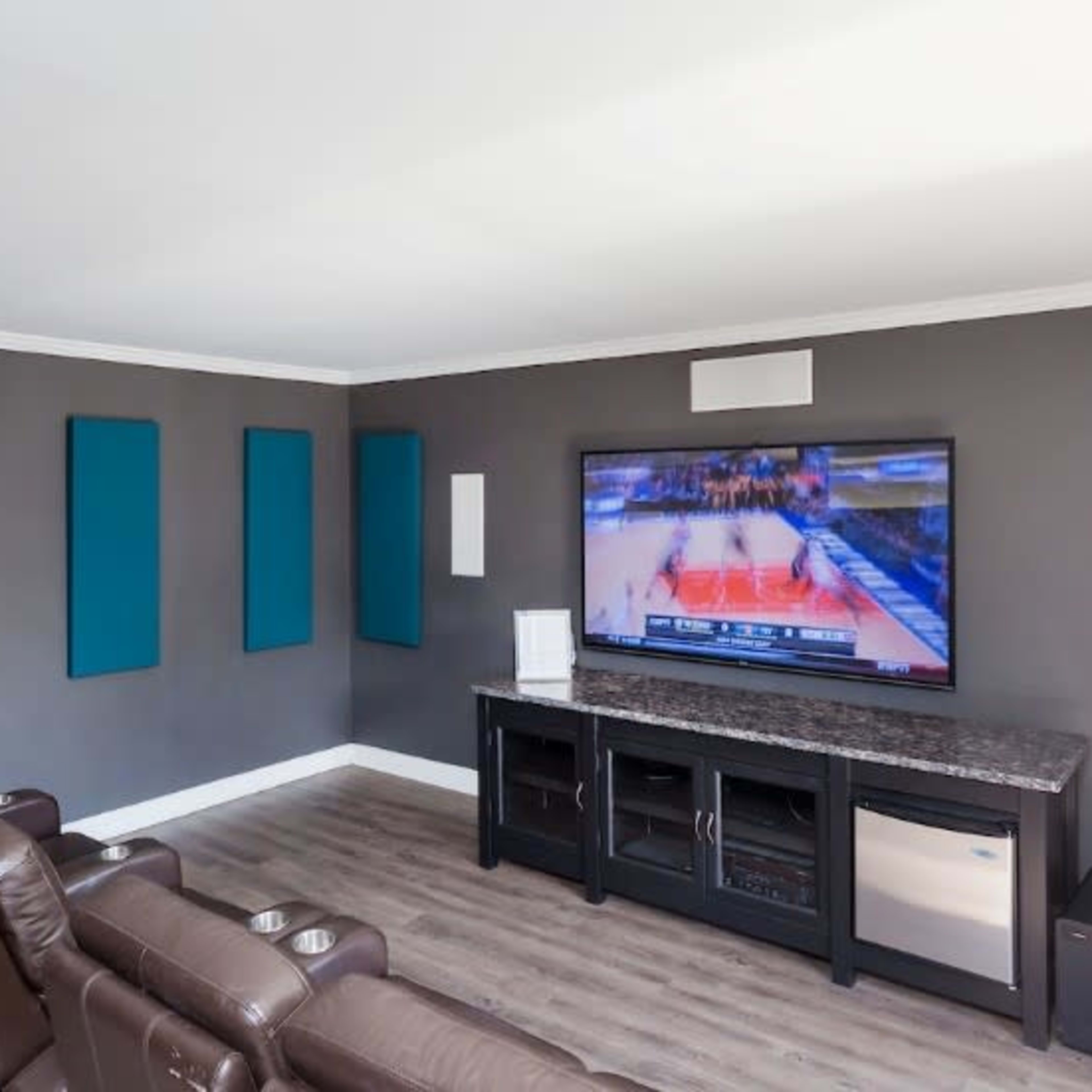 A modern living room features leather recliners facing a large flat-screen television mounted on a gray wall.