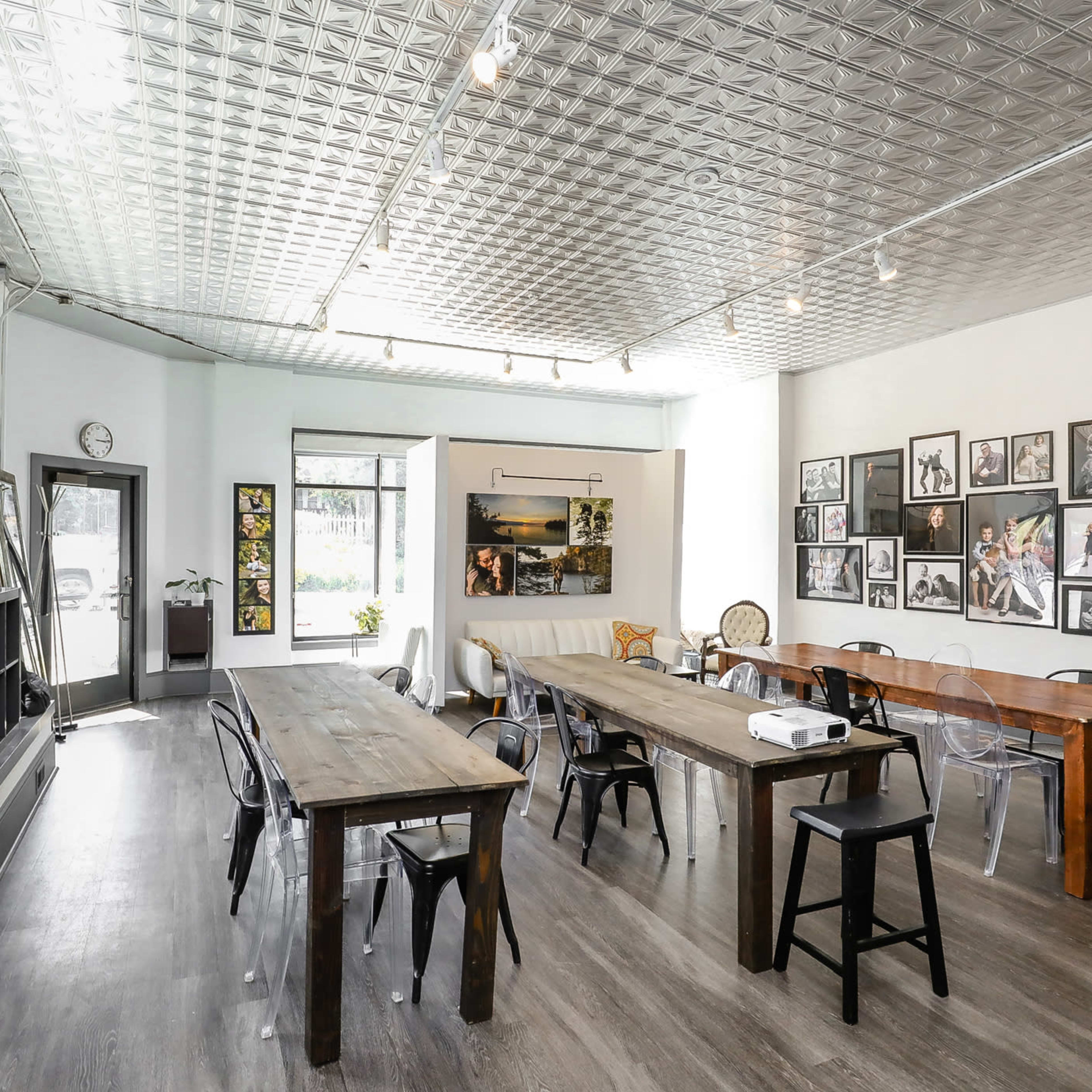 A bright, modern workspace with several wooden tables, a comfortable seating area, and a wall adorned with various framed photographs.