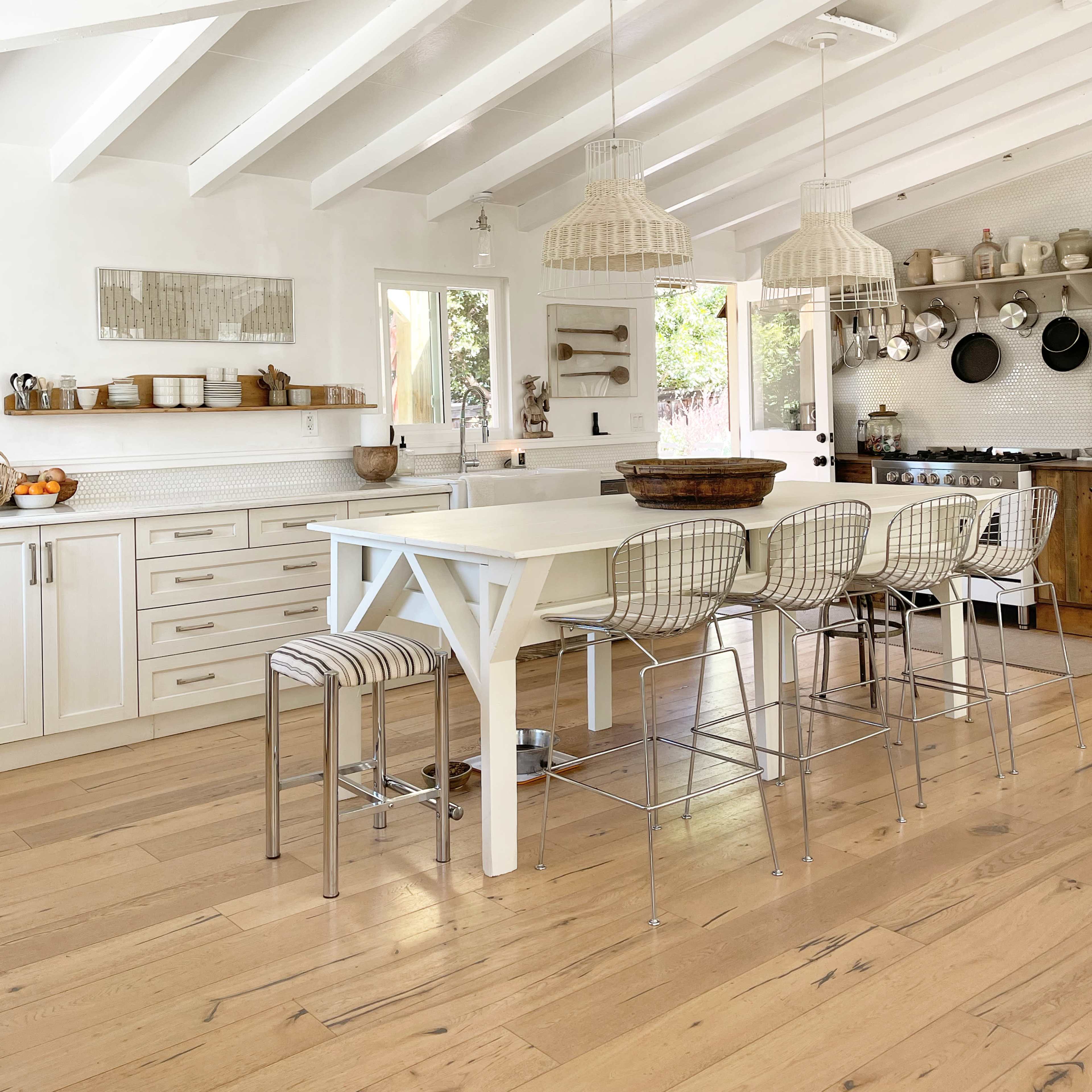 A bright kitchen features white cabinets, a large island with bar stools, and hanging light fixtures.