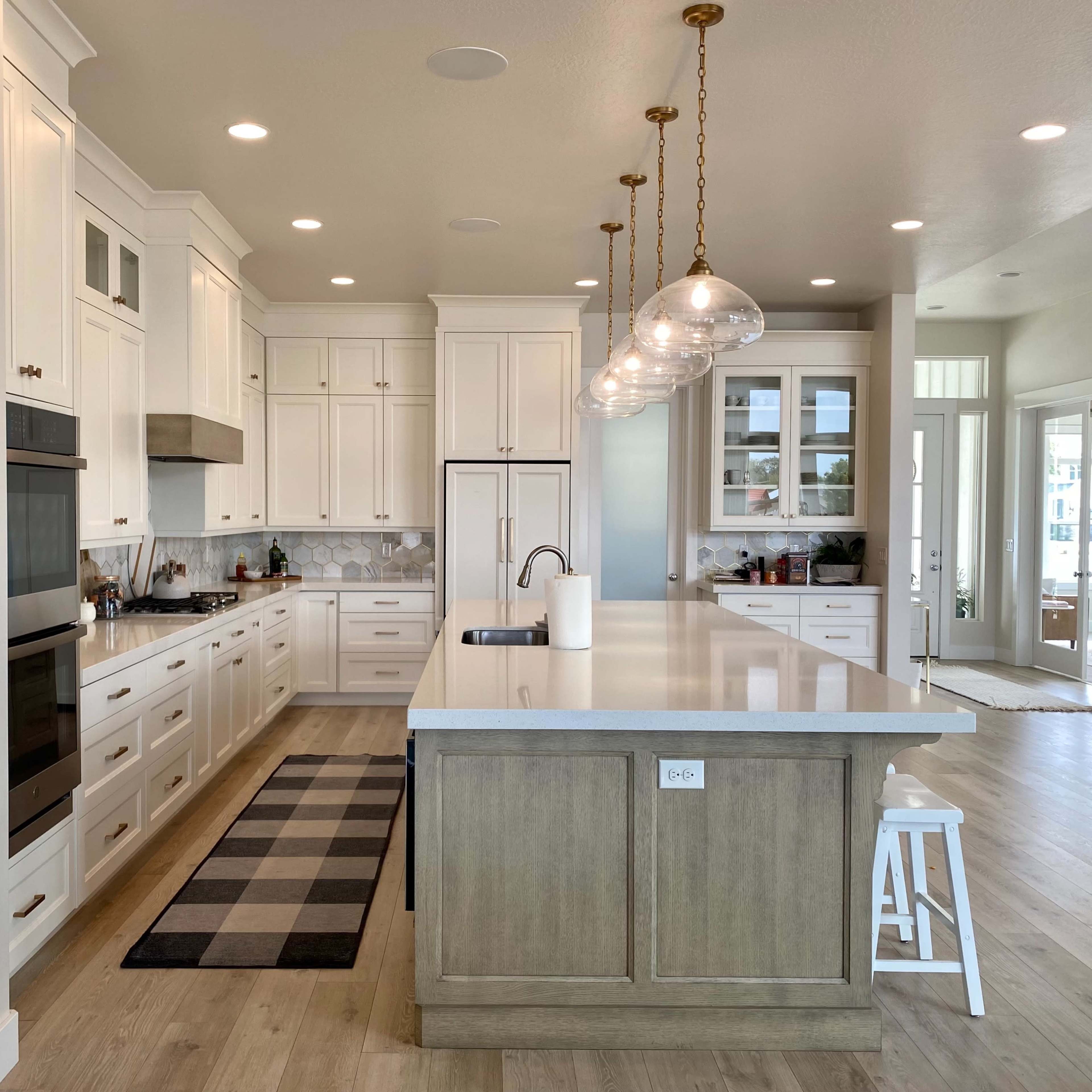 A modern kitchen features white cabinets, a large island with a light wood finish, and pendant lighting above the countertop.