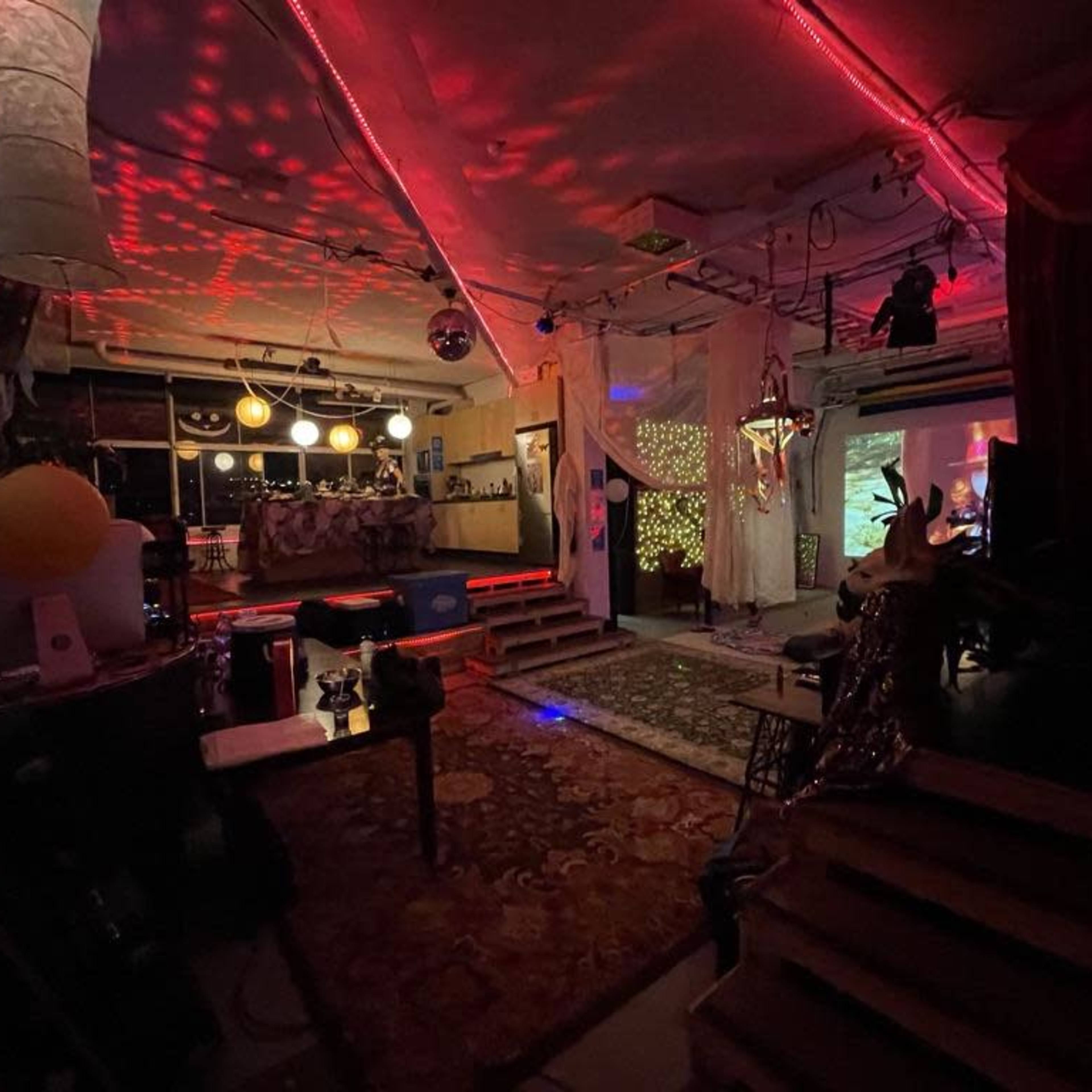 A dimly lit, eclectic interior space with colorful lights, patterned decorations, and various seating arrangements.