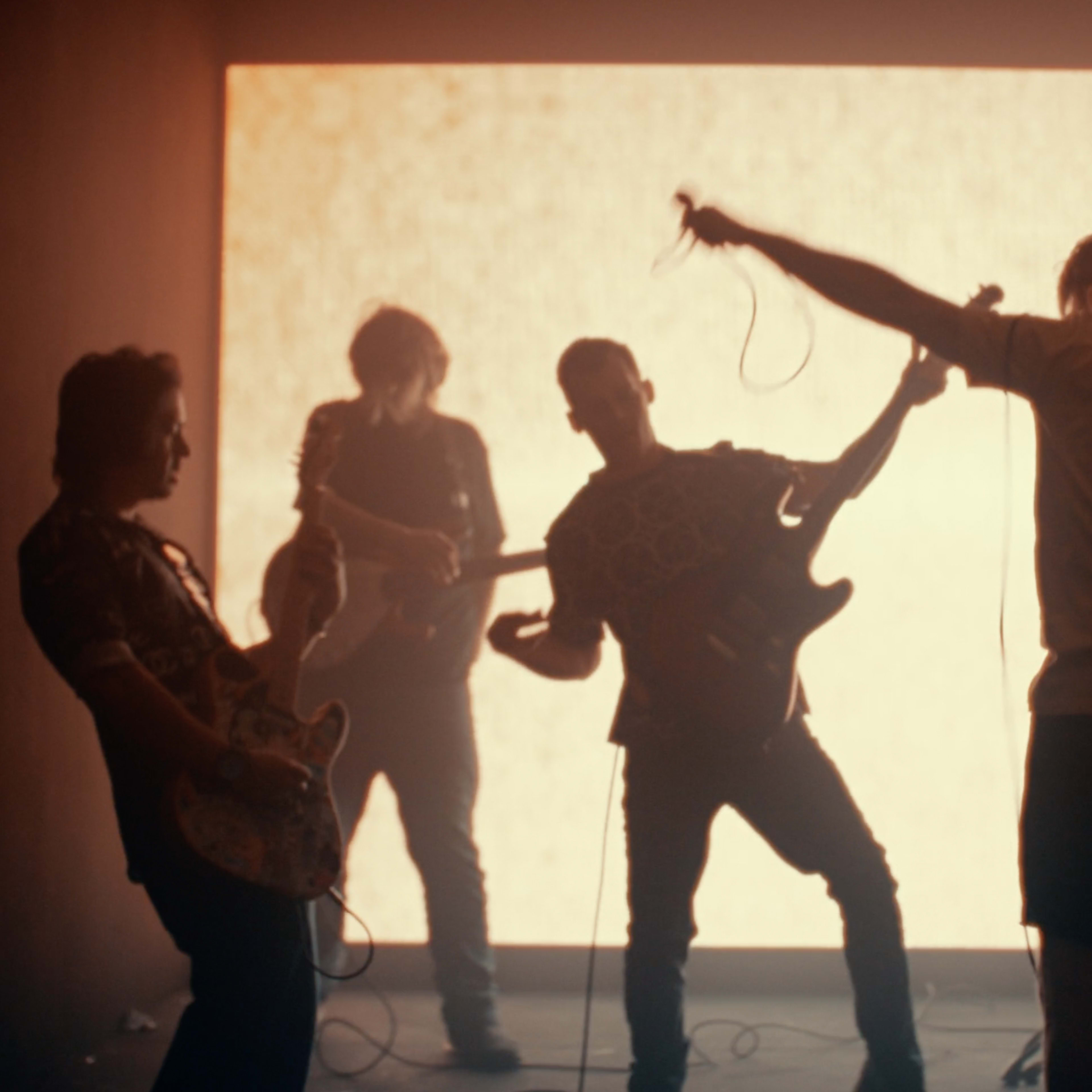 A band performs on stage in front of a bright backdrop, with members playing instruments and singing.