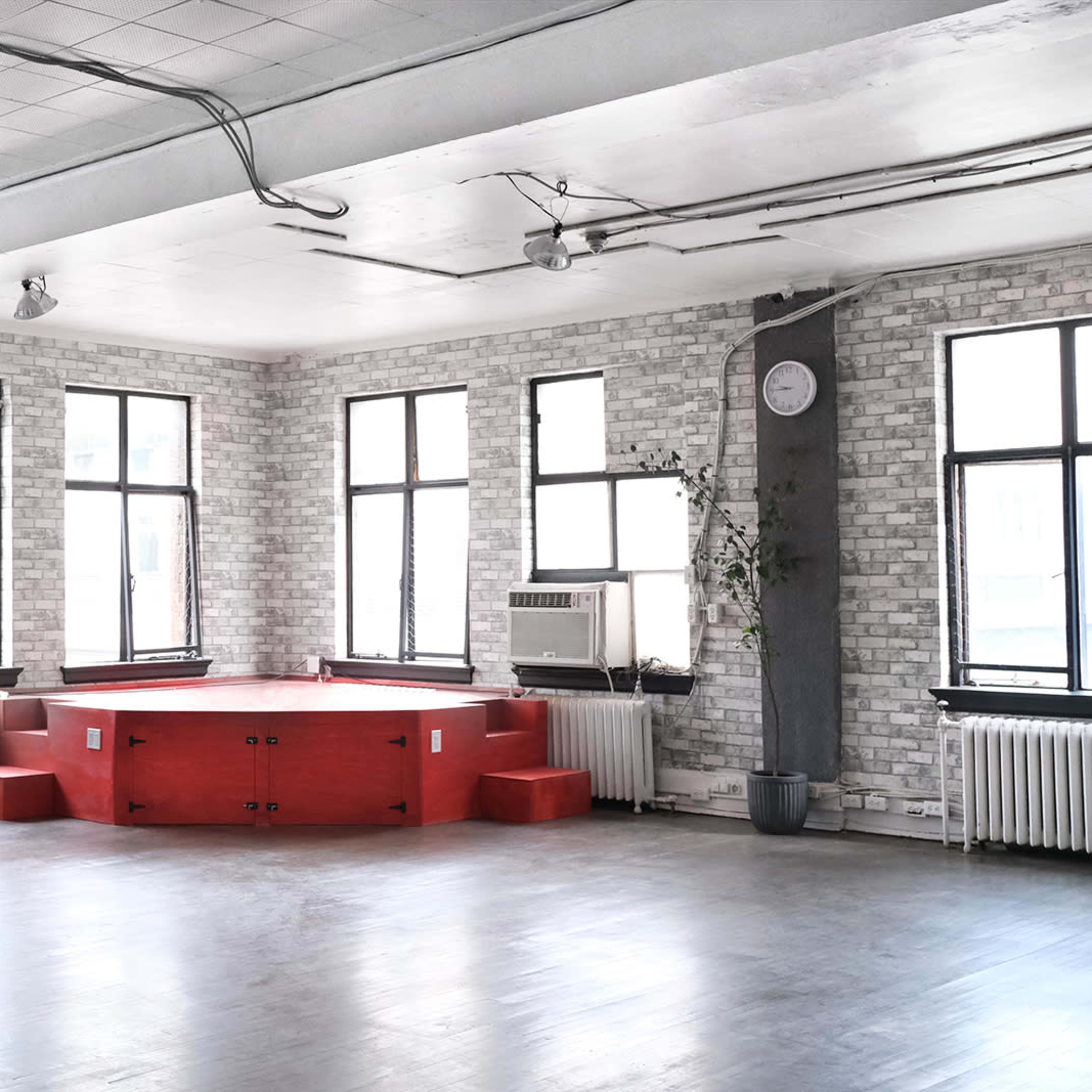 A spacious room with large windows, featuring a red platform in the center and industrial-style decor.