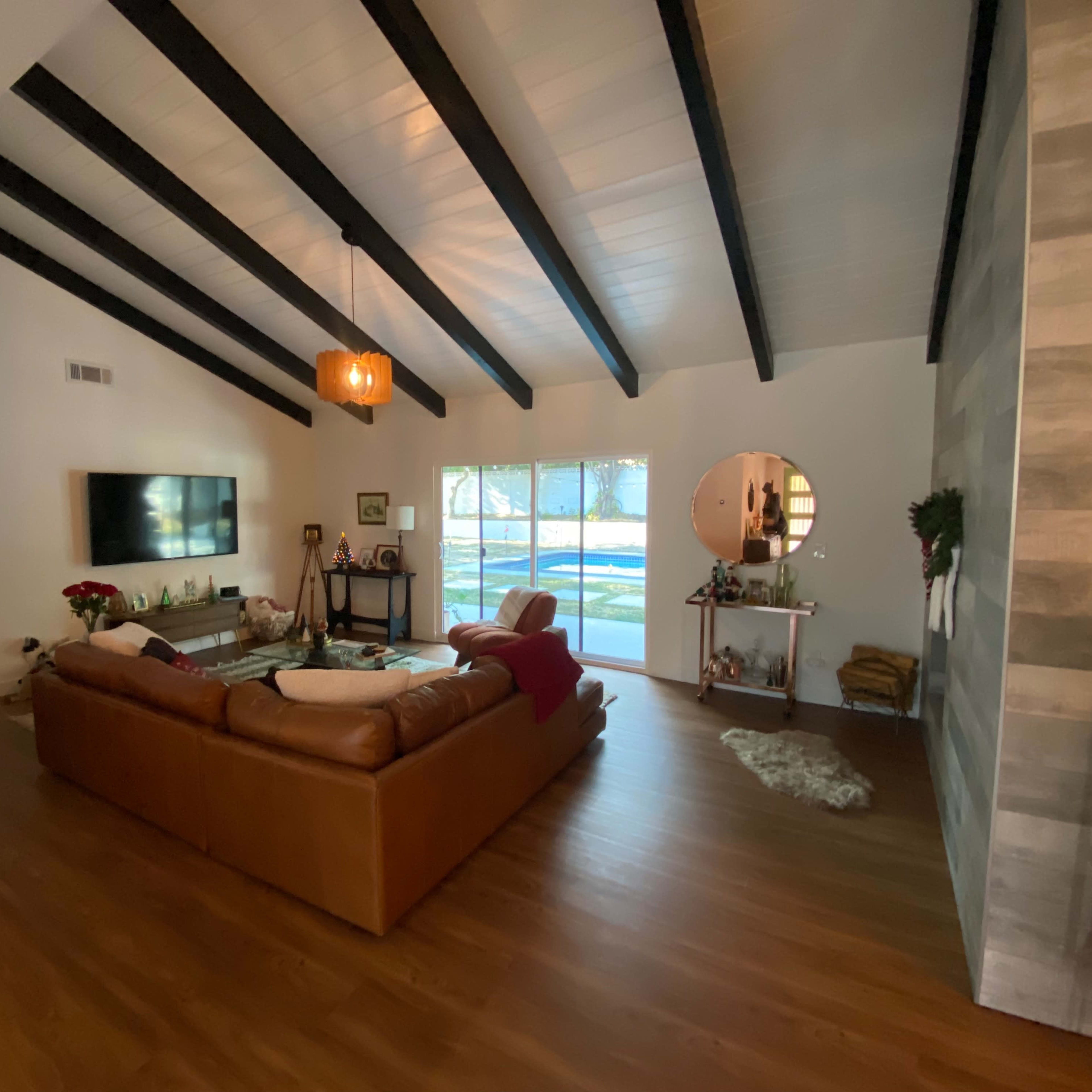 A living room with a high vaulted ceiling, featuring a brown leather sofa, large windows allowing natural light, and a small decorative table.