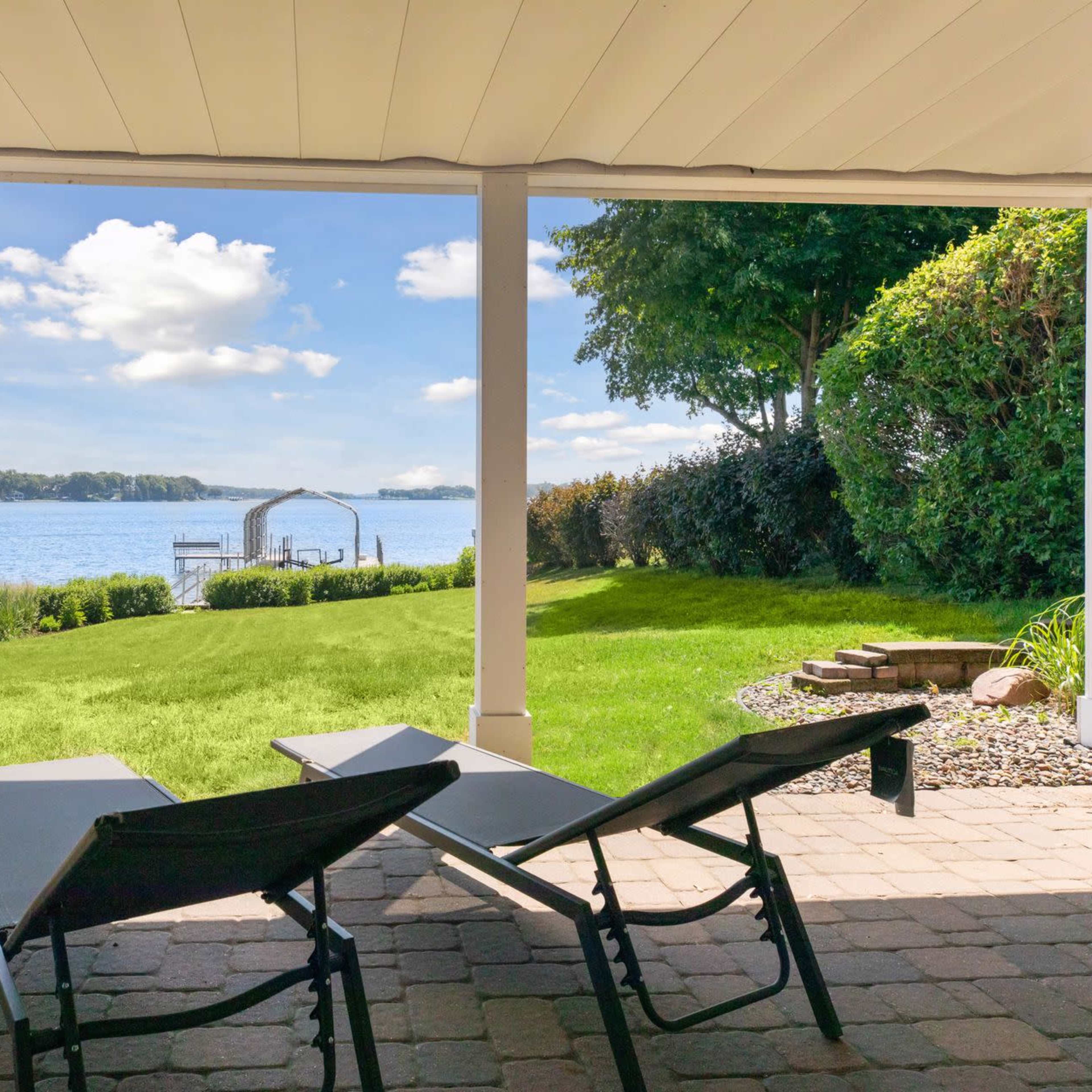A view of a lake from a patio area featuring two lounge chairs and manicured grass.