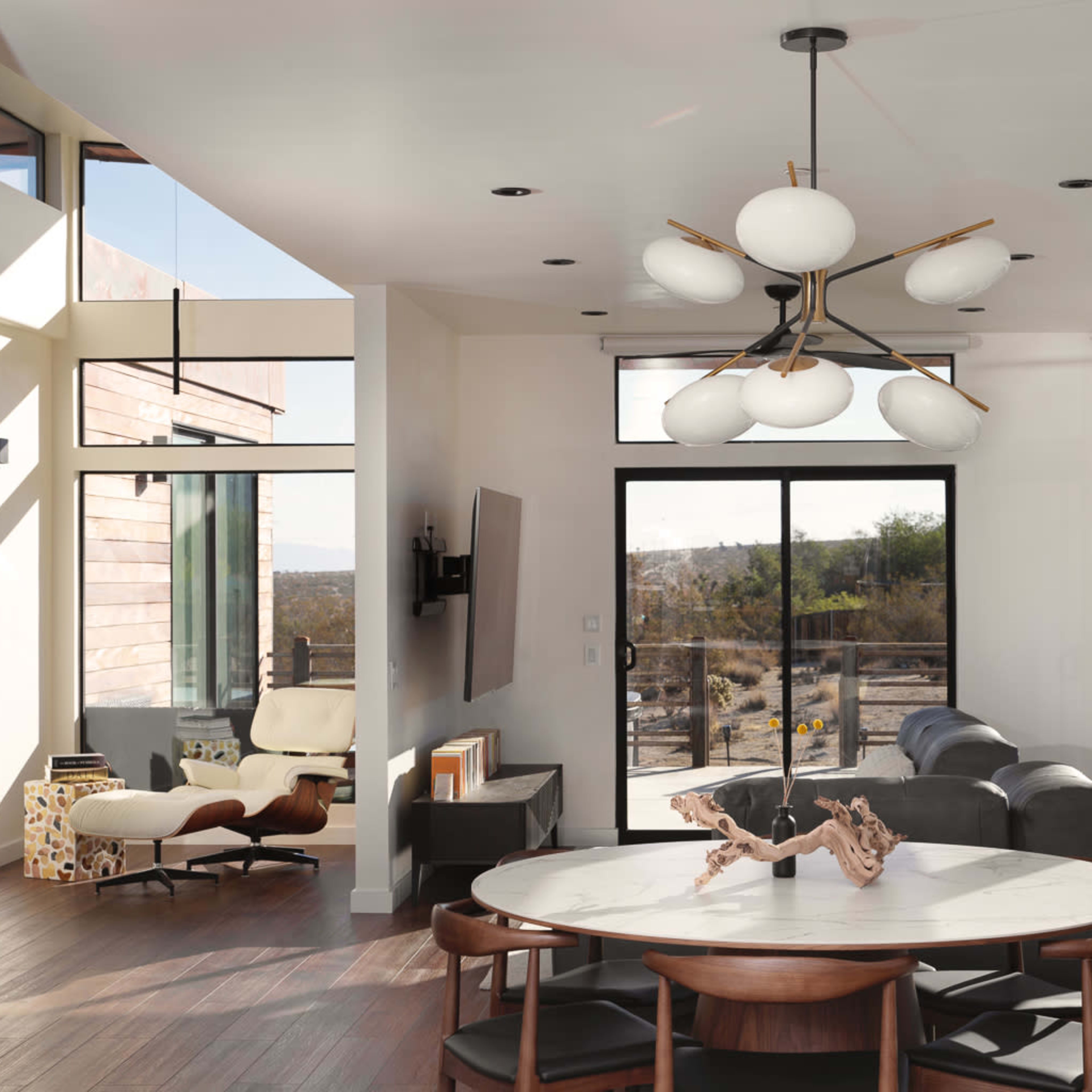 A modern living room with large windows, a round dining table, and a stylish light fixture.
