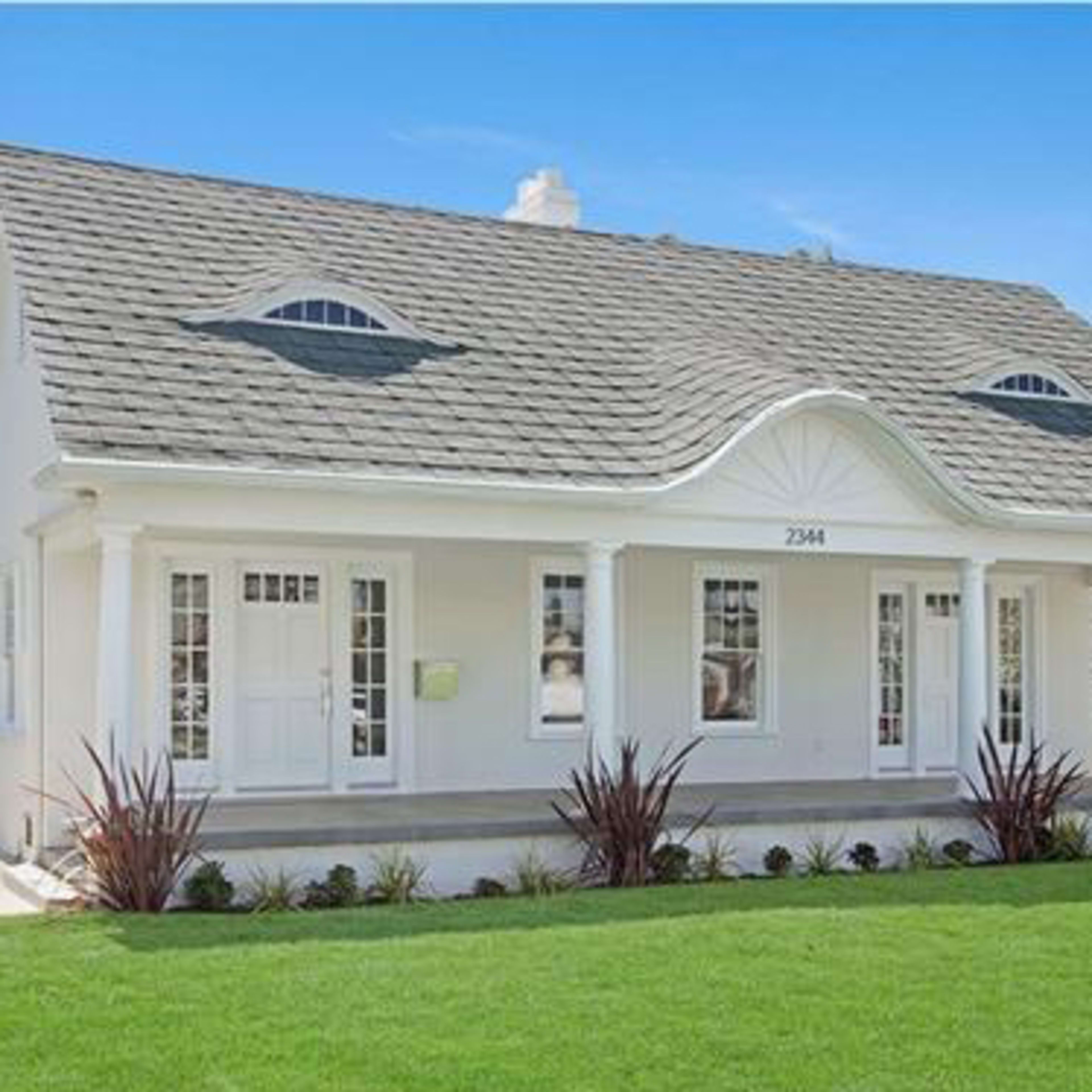A single-story white house with a distinctive curved roof, large front windows, and a well-manicured lawn.