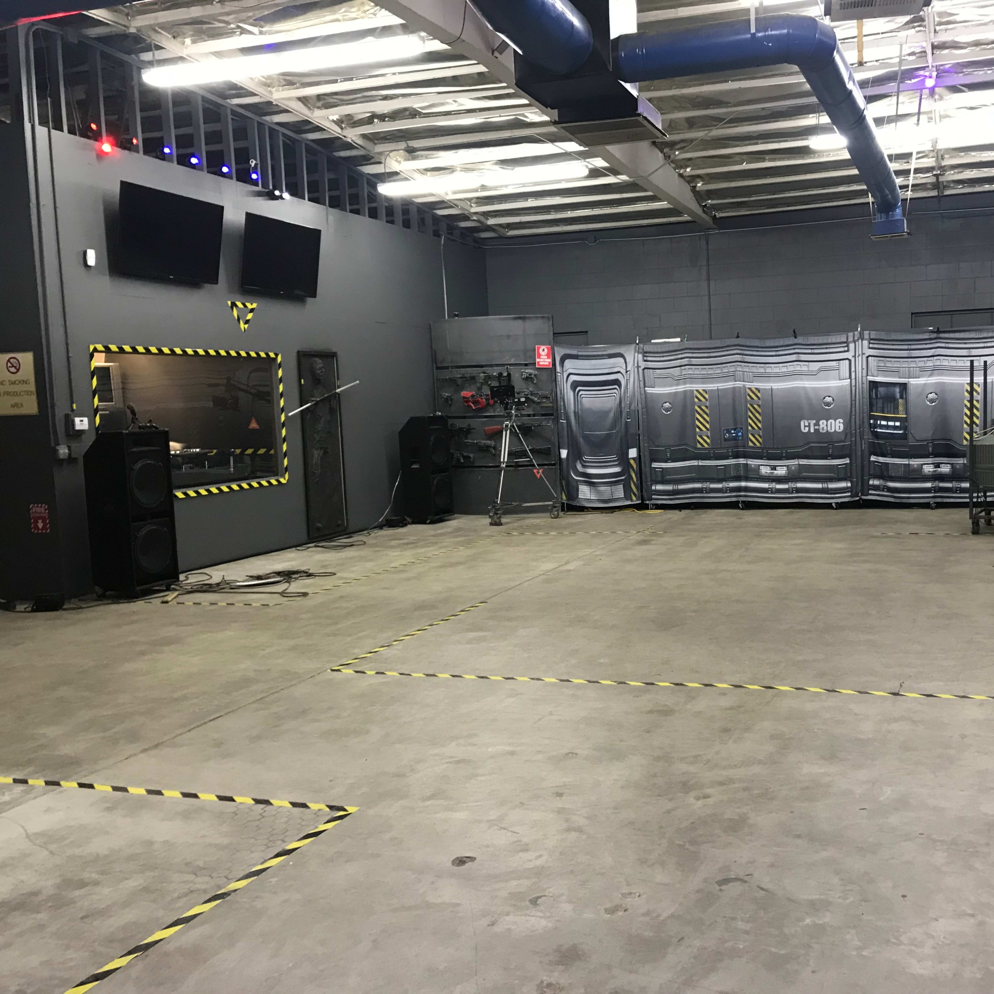 An industrial-style room with a concrete floor, equipped with audio equipment, cameras, and a backdrop resembling a futuristic setting.