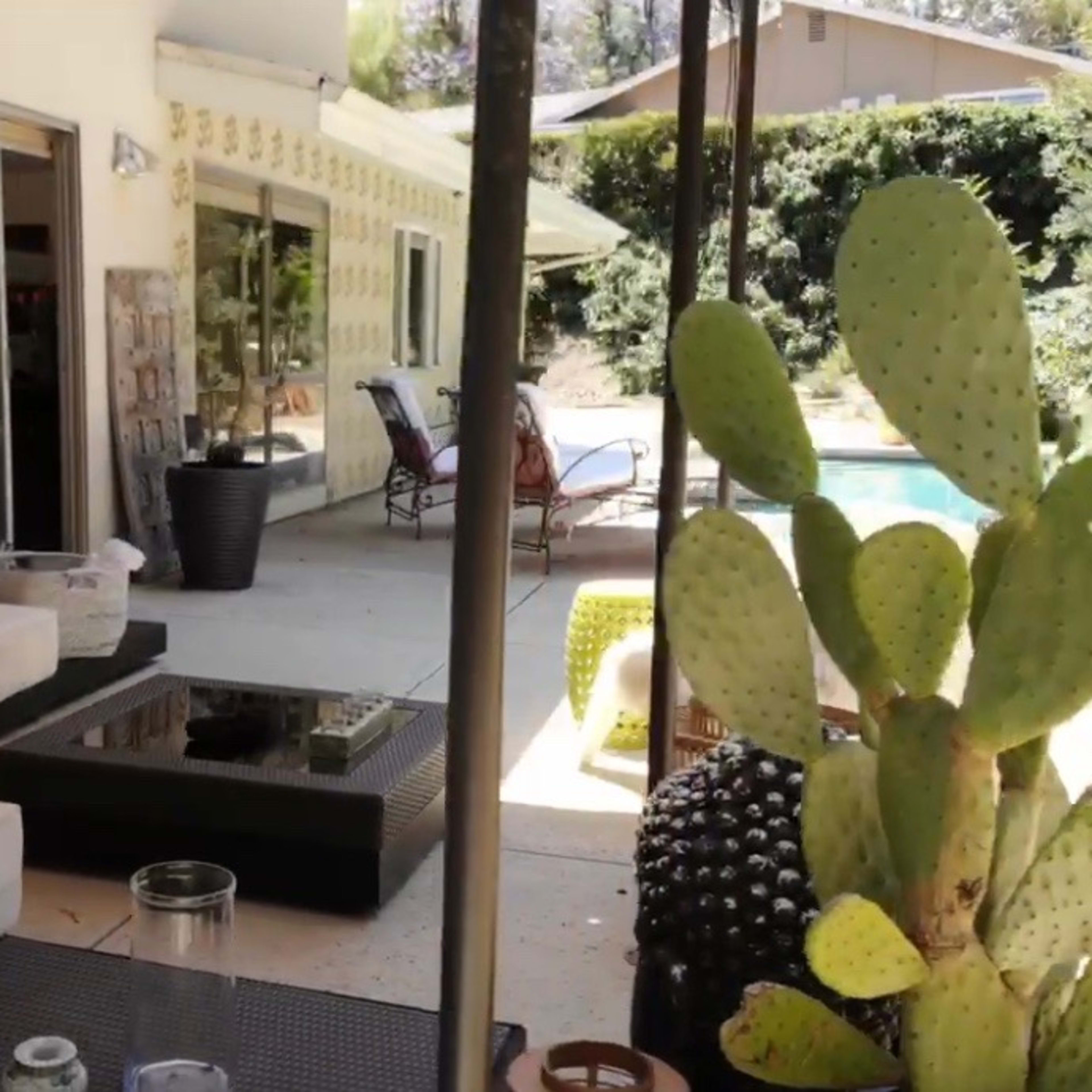 A patio area features a modern seating arrangement, coffee table, and a cactus plant, all adjacent to a swimming pool.