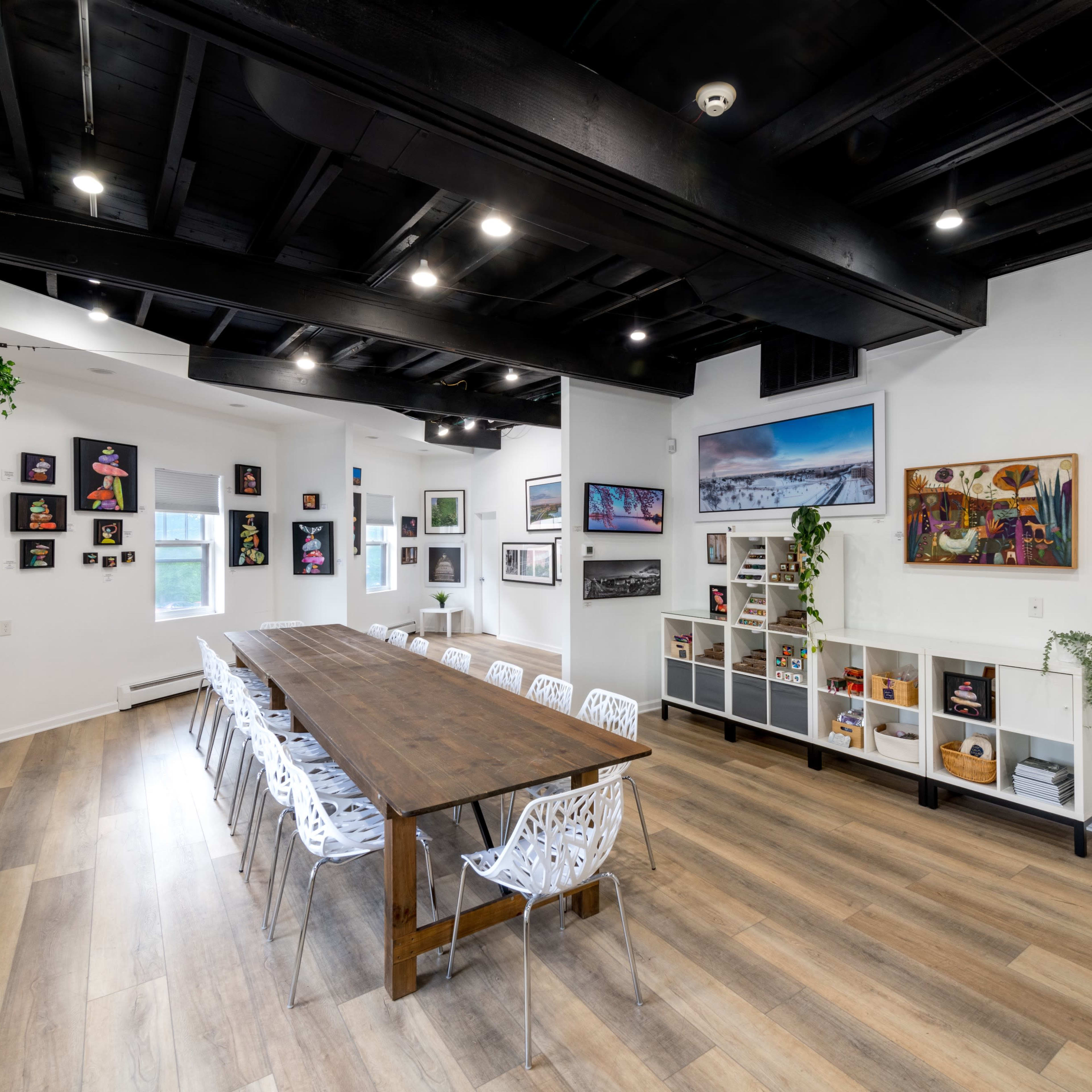 A spacious meeting room with a large wooden table surrounded by white chairs, adorned with artwork on the walls and natural light coming through the windows.