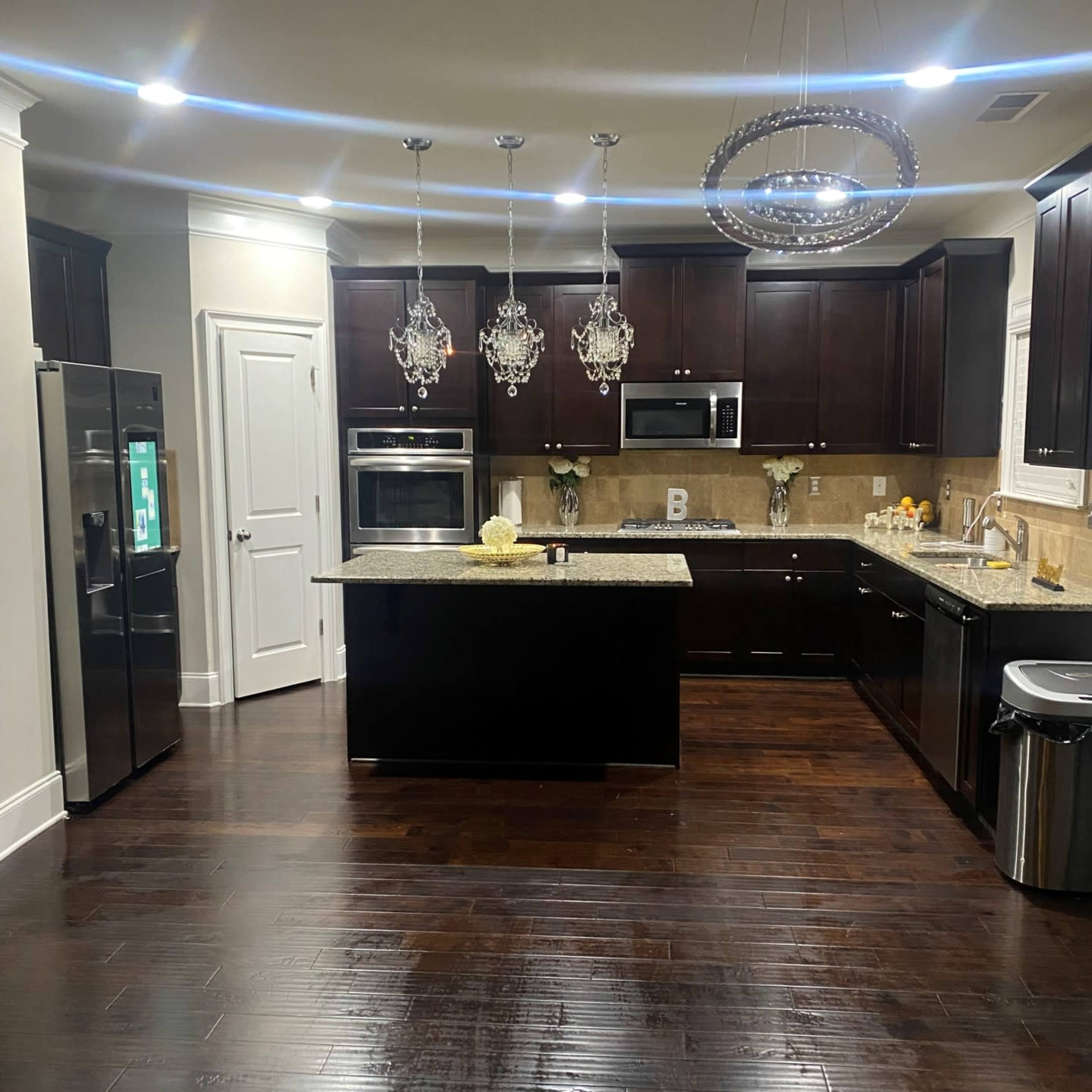 The kitchen features dark wooden cabinets, a central island with a granite countertop, and modern appliances, illuminated by pendant lights.
