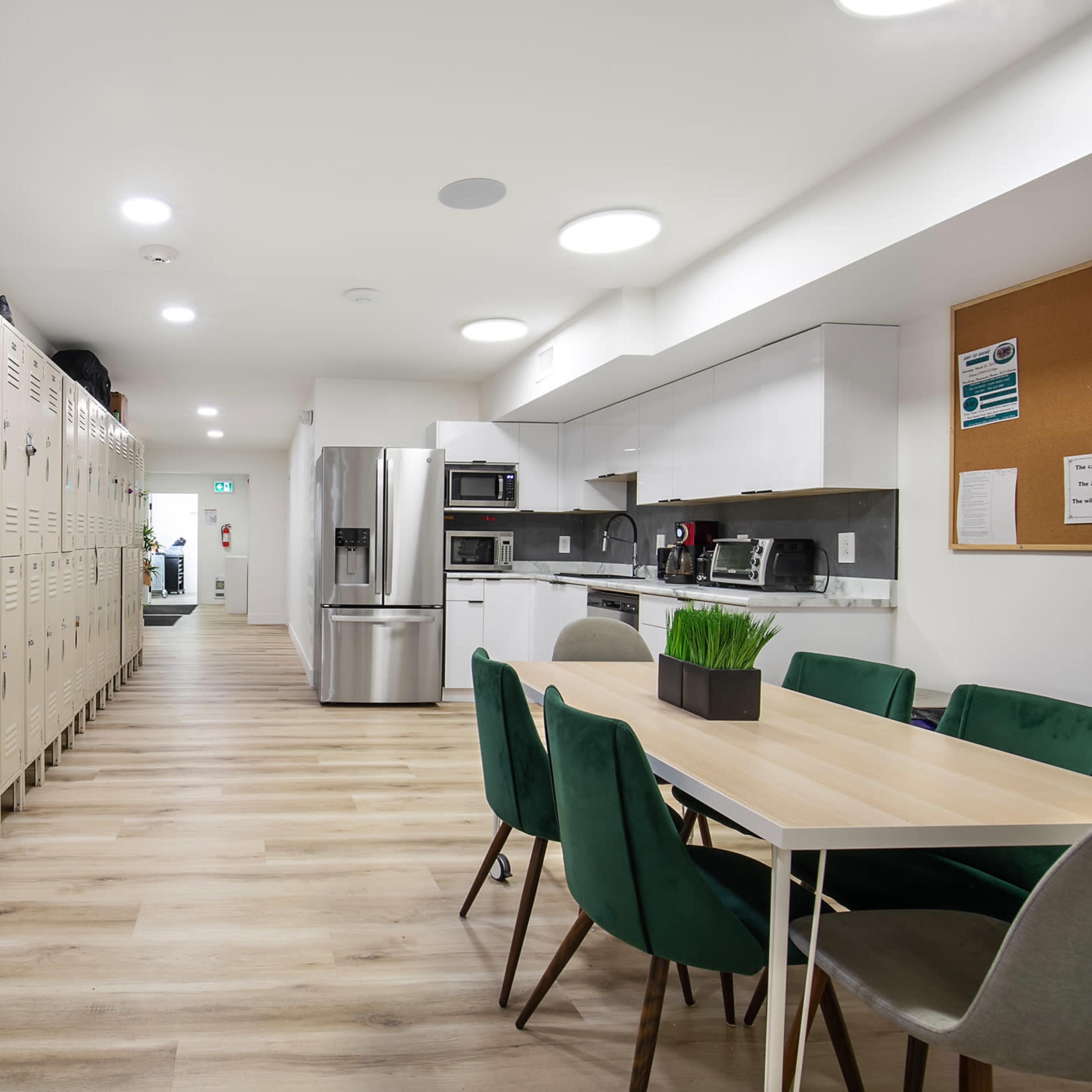 A modern kitchen and dining area with lockers on one side and a table surrounded by chairs on the other.