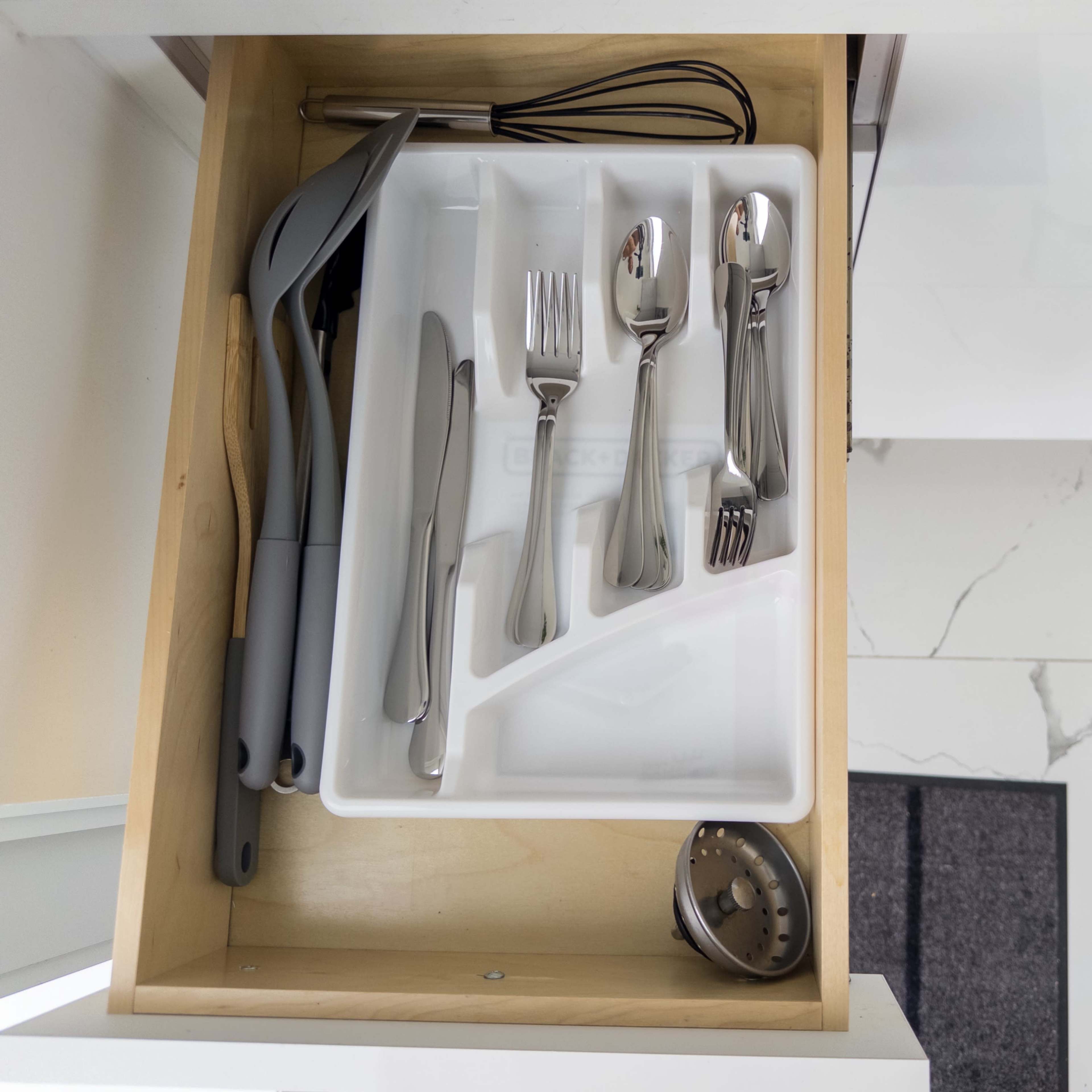 A kitchen drawer contains a utensil organizer with various silverware, a whisk, and cooking tools.