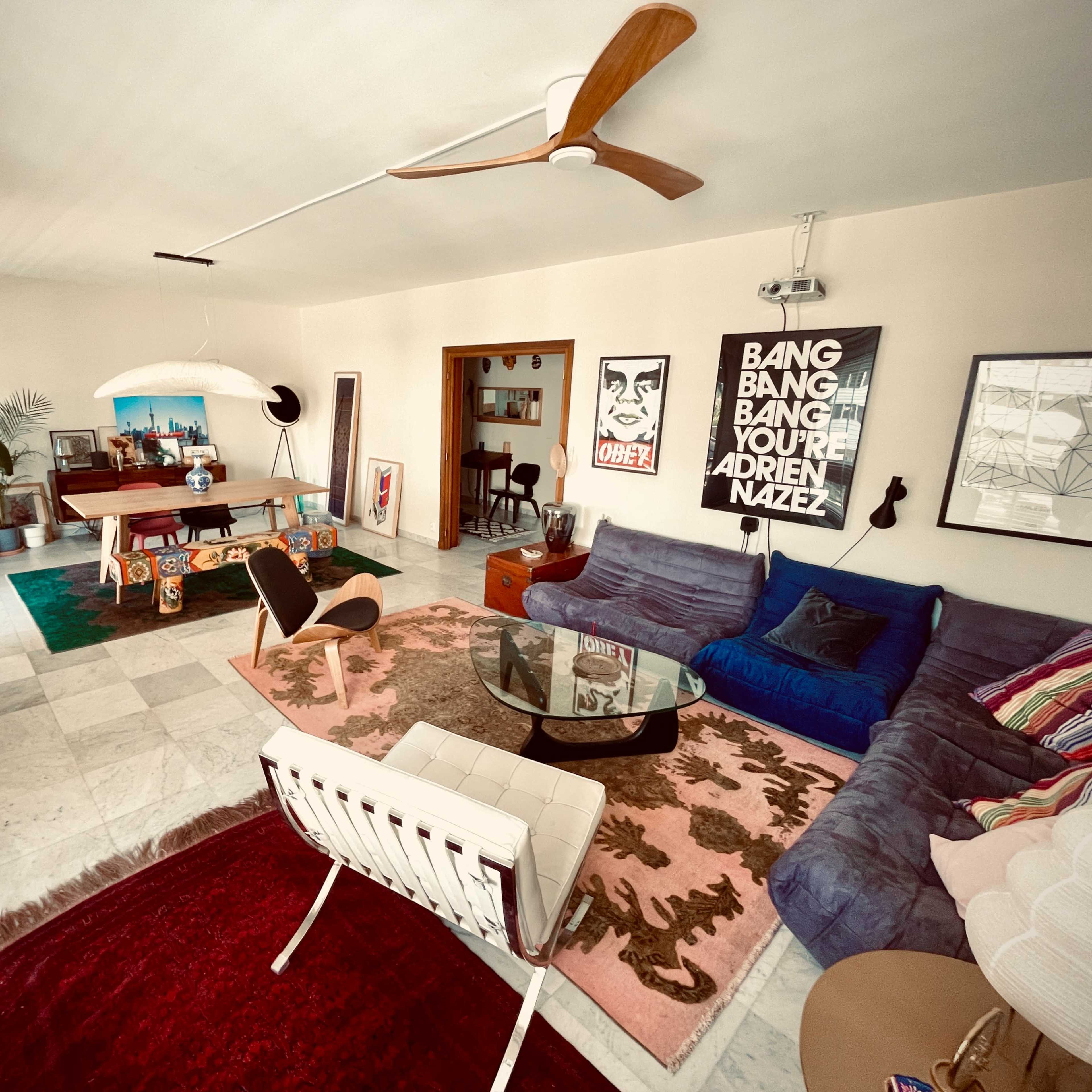 A stylish living room with a blue sectional sofa, a glass coffee table, and various artworks on the walls.