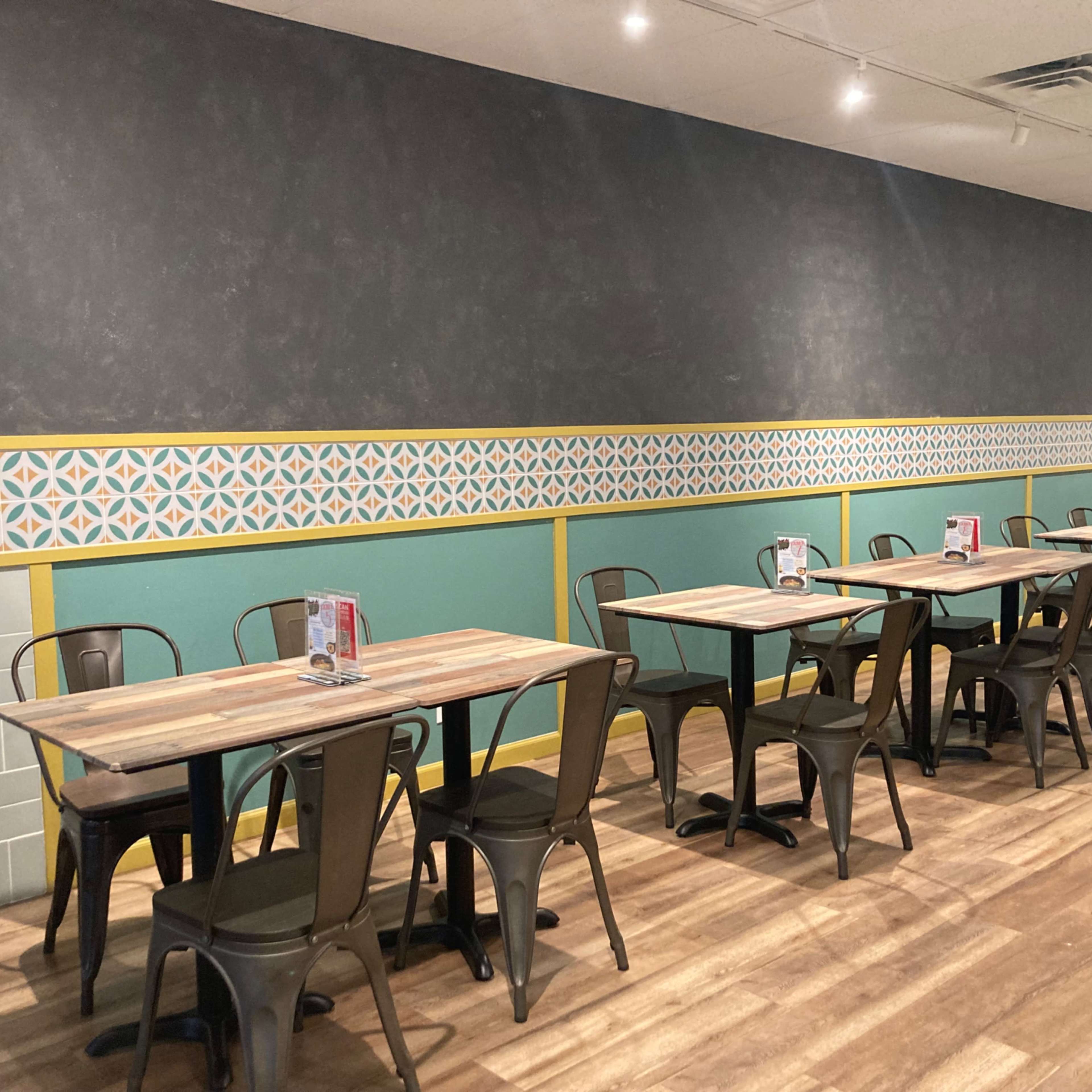 A modern restaurant interior with several wooden tables and metal chairs arranged neatly against a patterned wall.