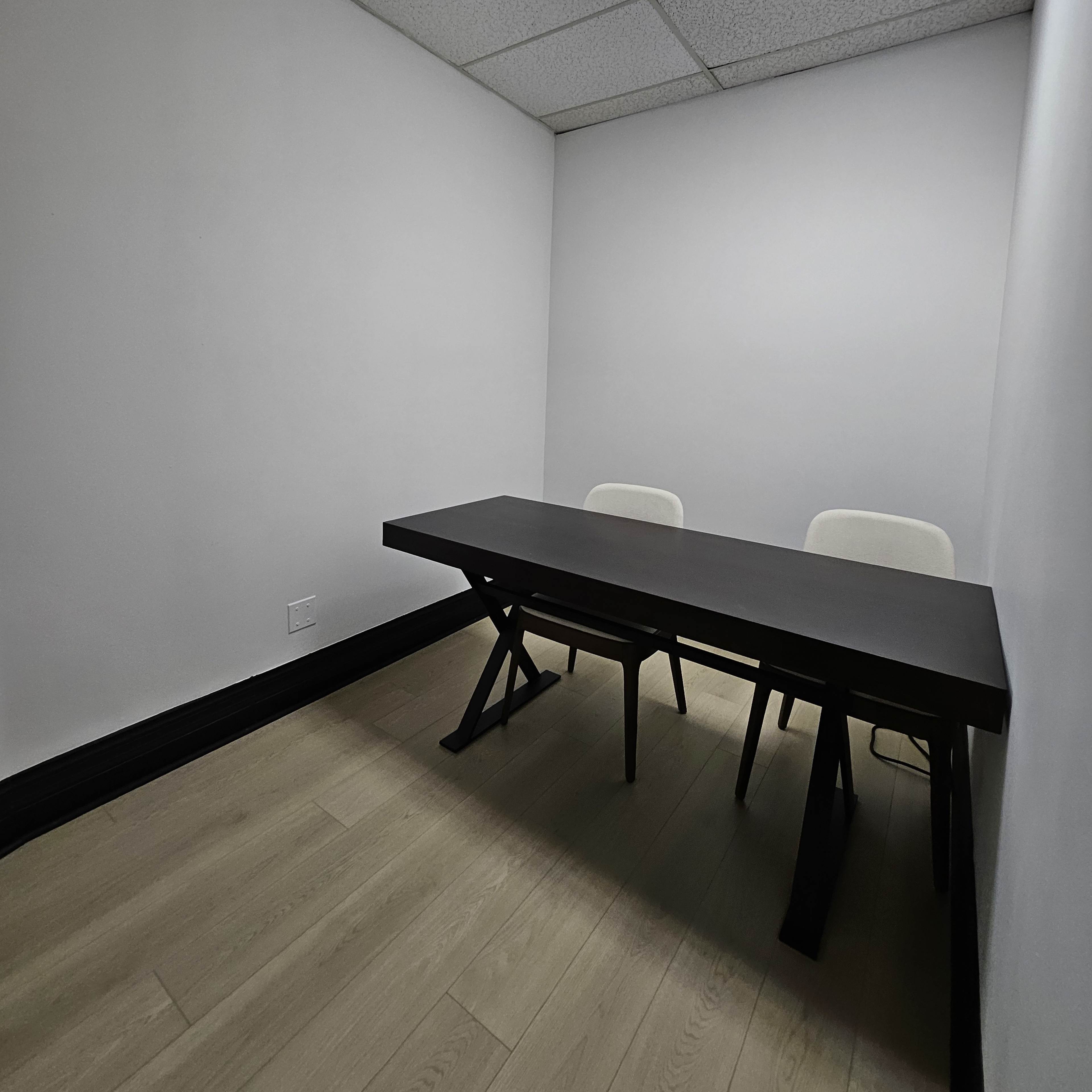 A small, empty meeting room with a black table and two white chairs against a plain white wall.