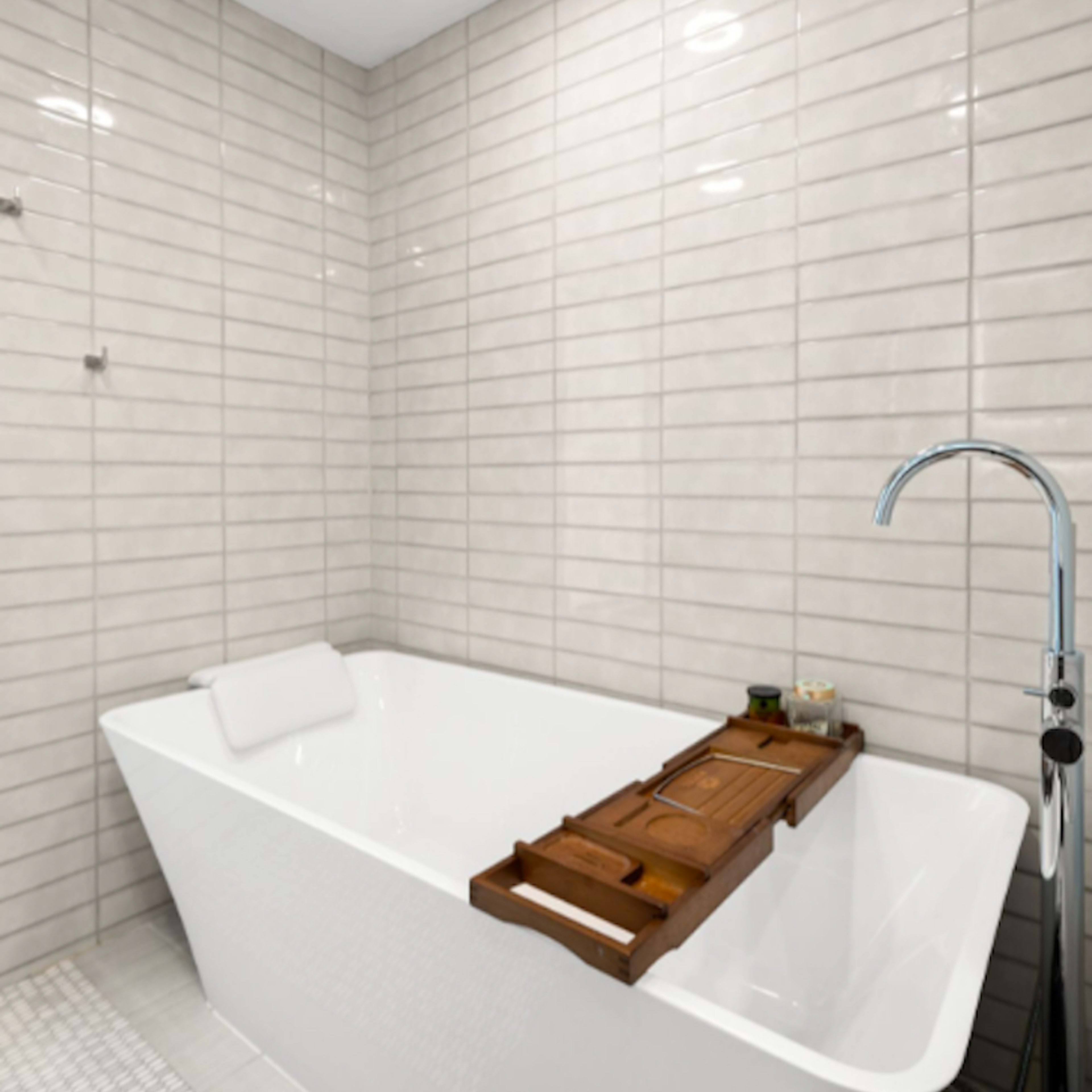 A modern bathroom featuring a freestanding white bathtub with a wooden tray resting on the edge, set against light gray tiled walls.