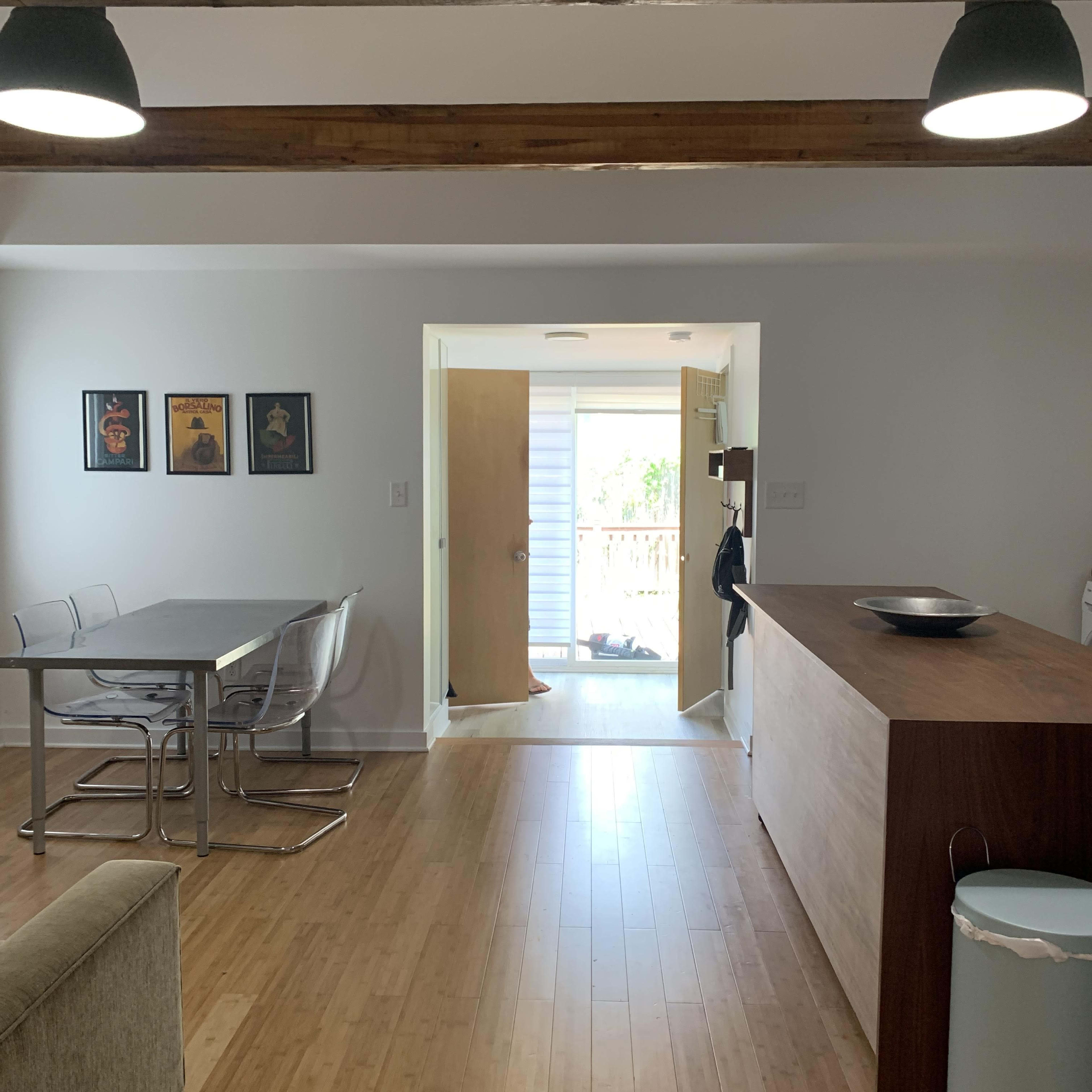 A modern, open-concept living space featuring a dining table with chairs, a wooden countertop, and a doorway leading to a deck outside.