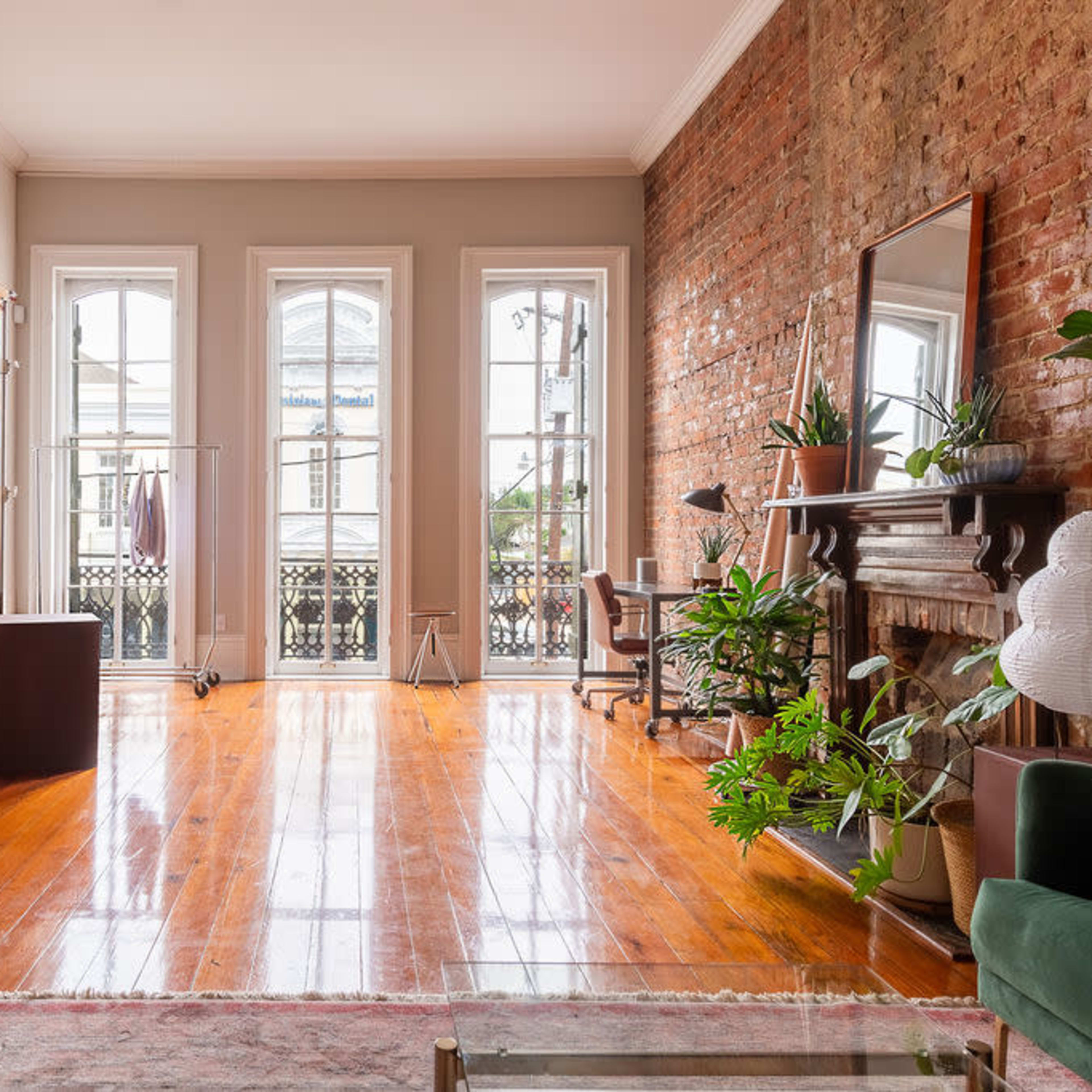 A spacious room with large windows, hardwood floors, a brick wall, a backdrop stand, and a mirror.