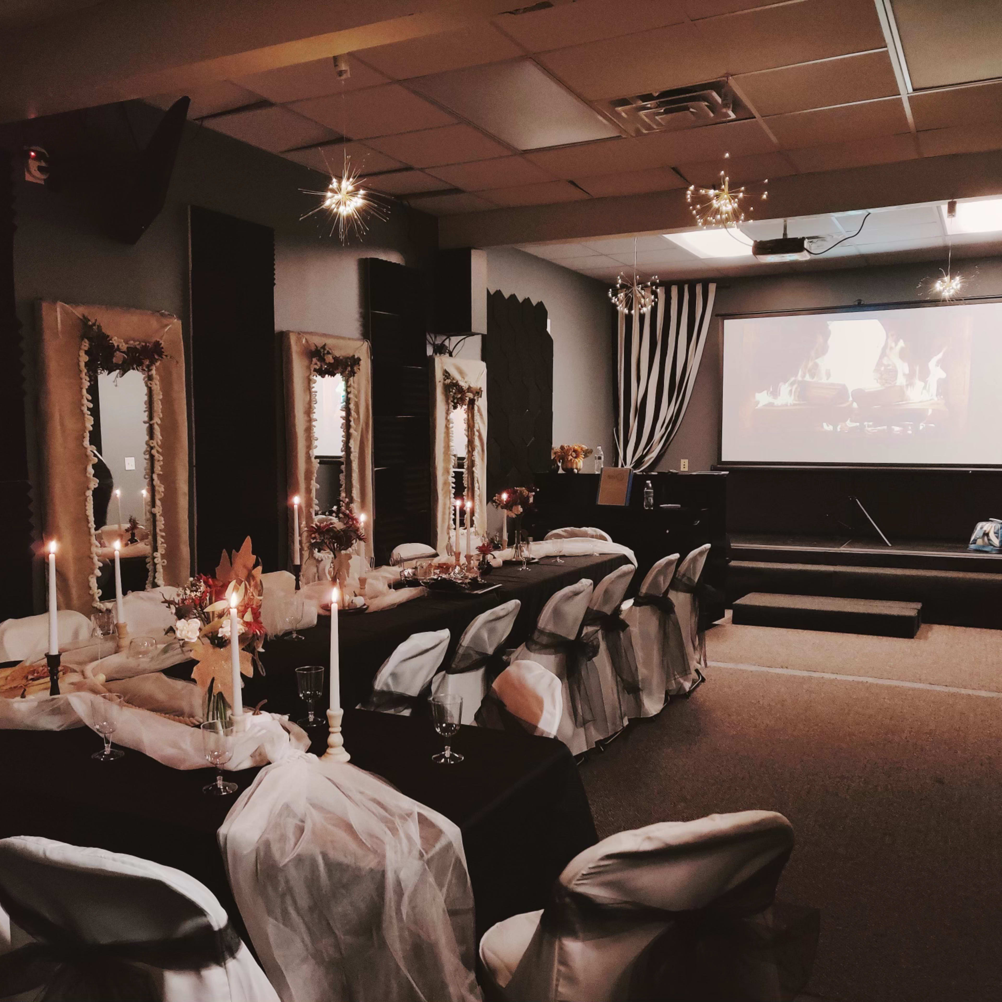 A long banquet table is set with white and black decor, surrounded by chairs, with a projector screen displaying a fire image in the background.