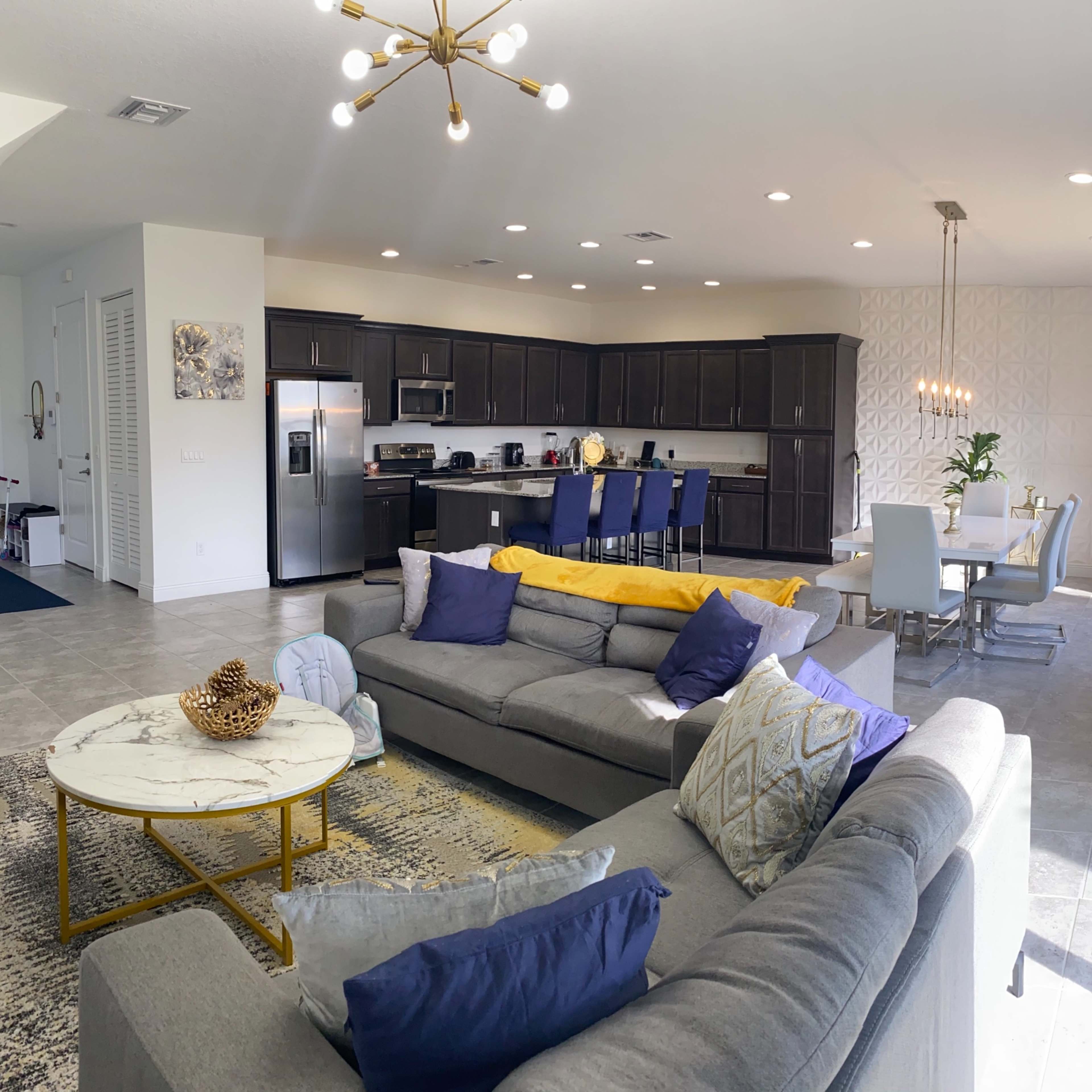 A modern living area with a gray sectional sofa, a marble coffee table, and an adjacent dining space featuring a rectangular table with white chairs.
