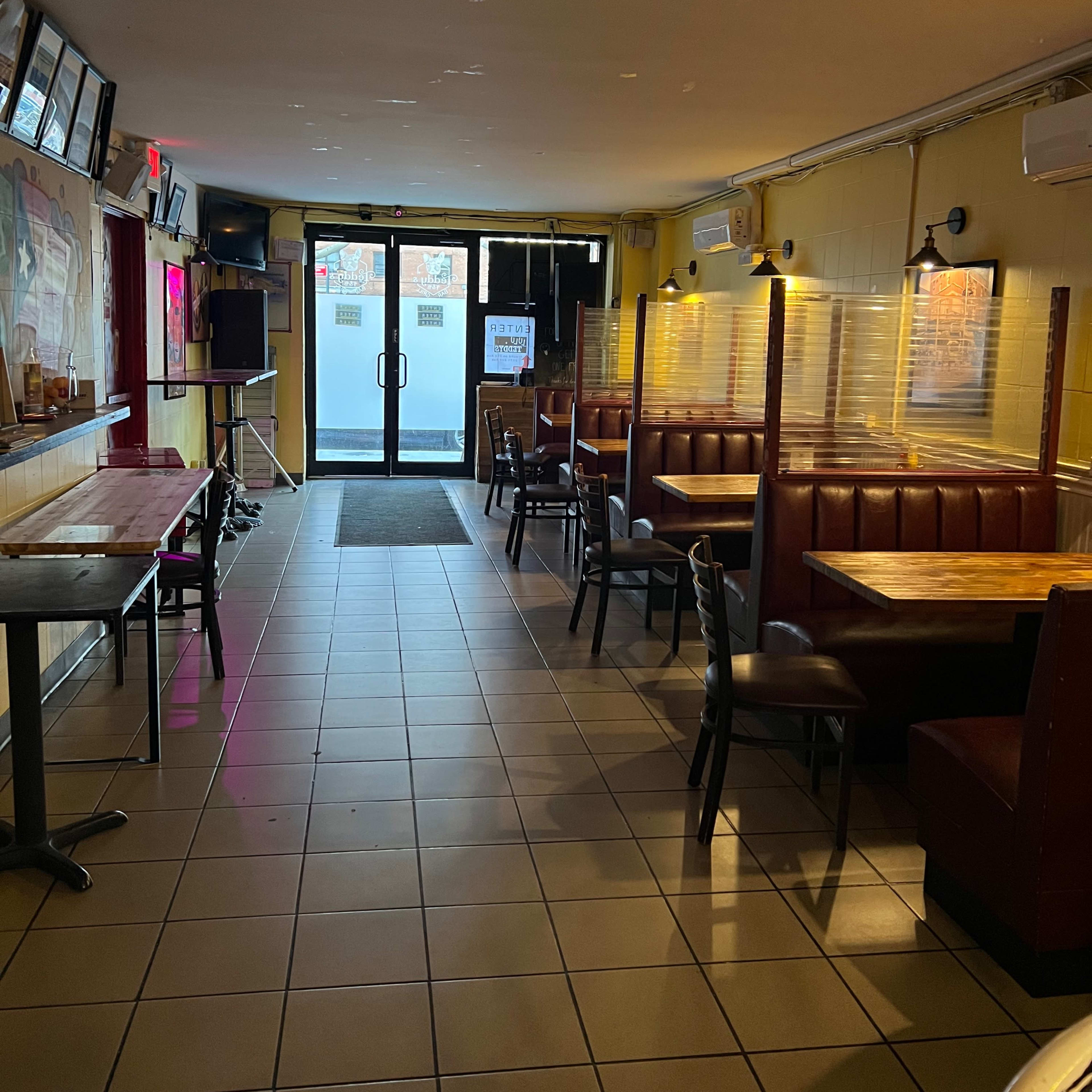 A partially empty restaurant interior featuring booths on one side and tables on the other, with a glass door at the far end leading outside.