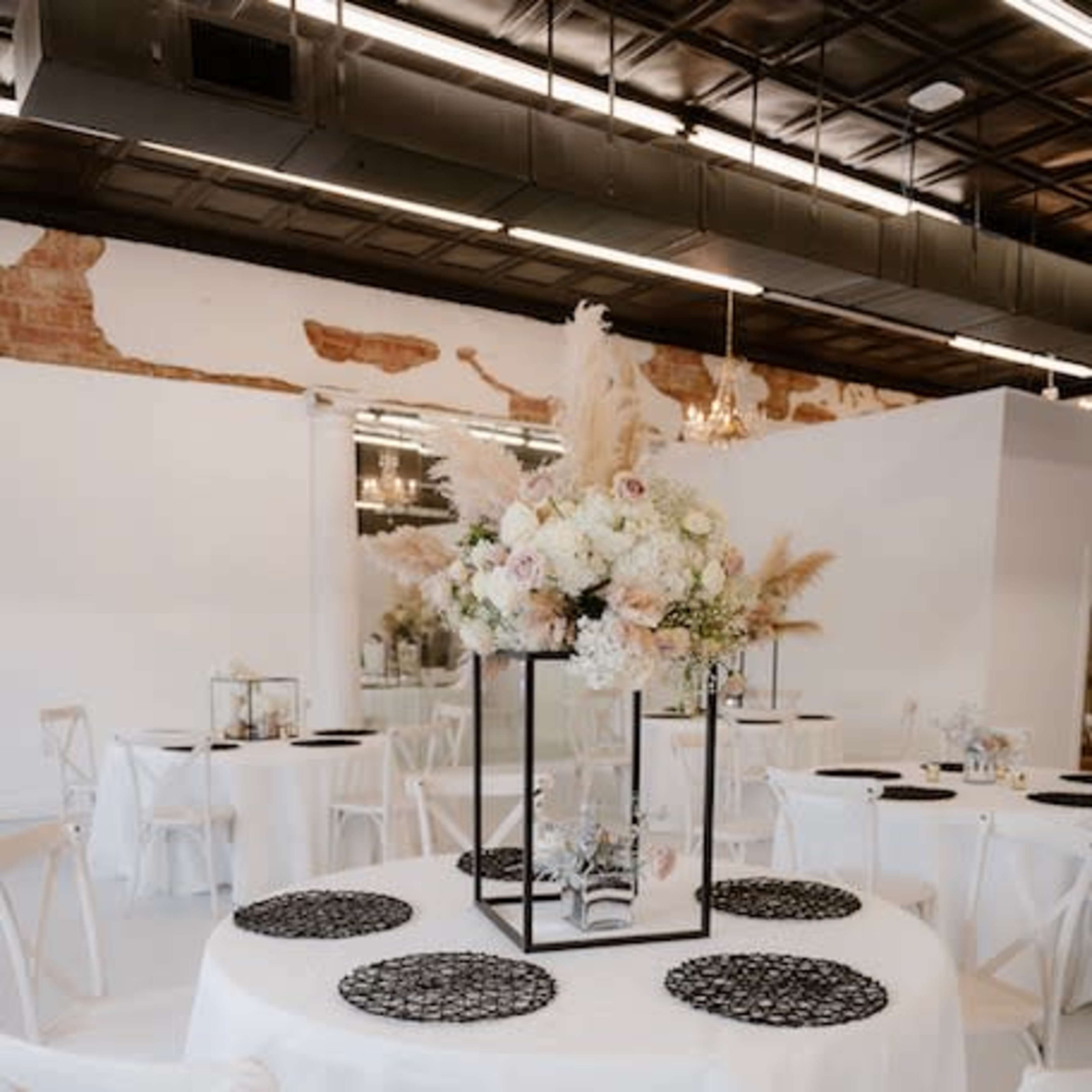 A modern banquet hall set with round tables covered in white tablecloths, featuring floral centerpieces and decorative place settings.