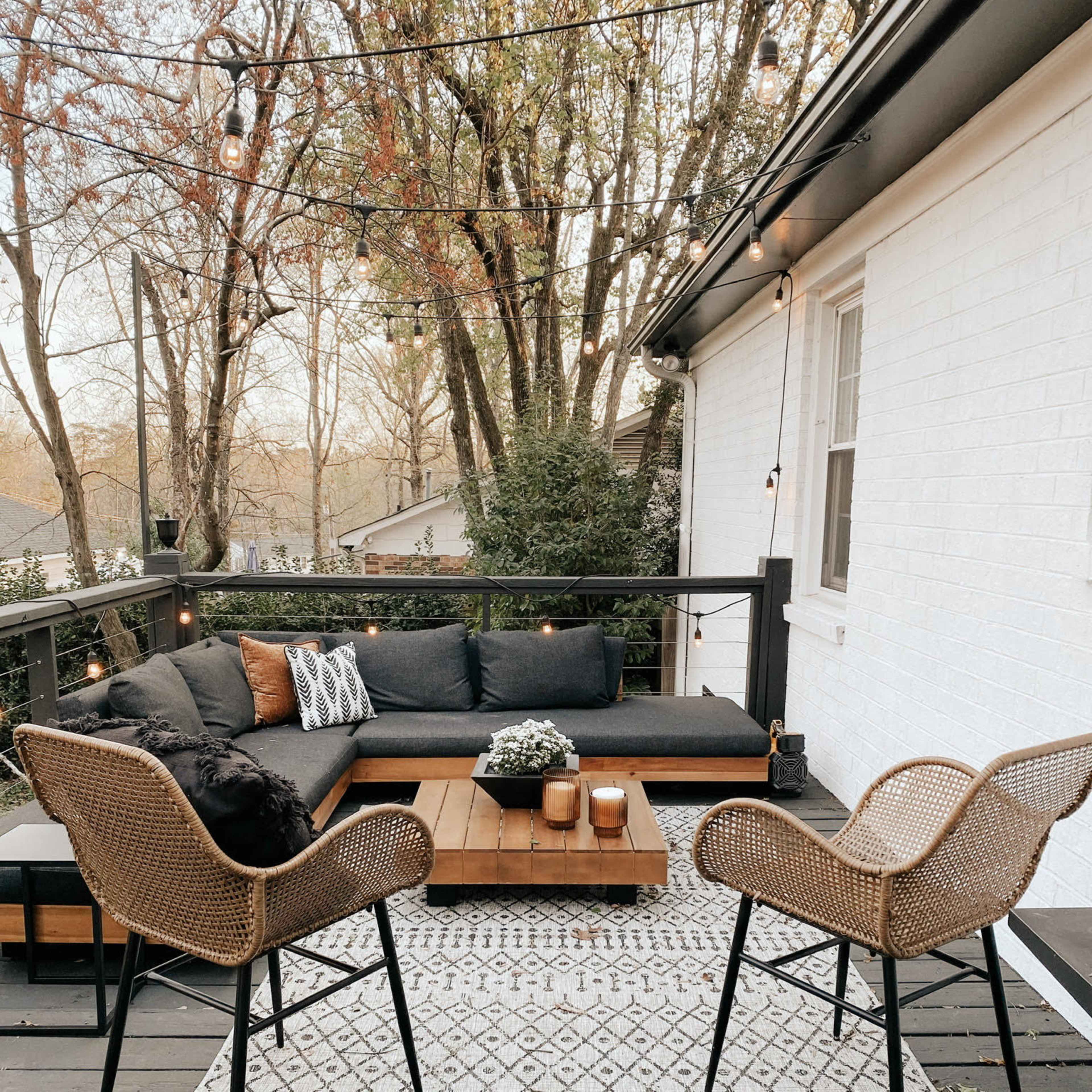 A bright sunroom features large windows, a cozy sofa, a leather chair, and various plants arranged throughout the space.