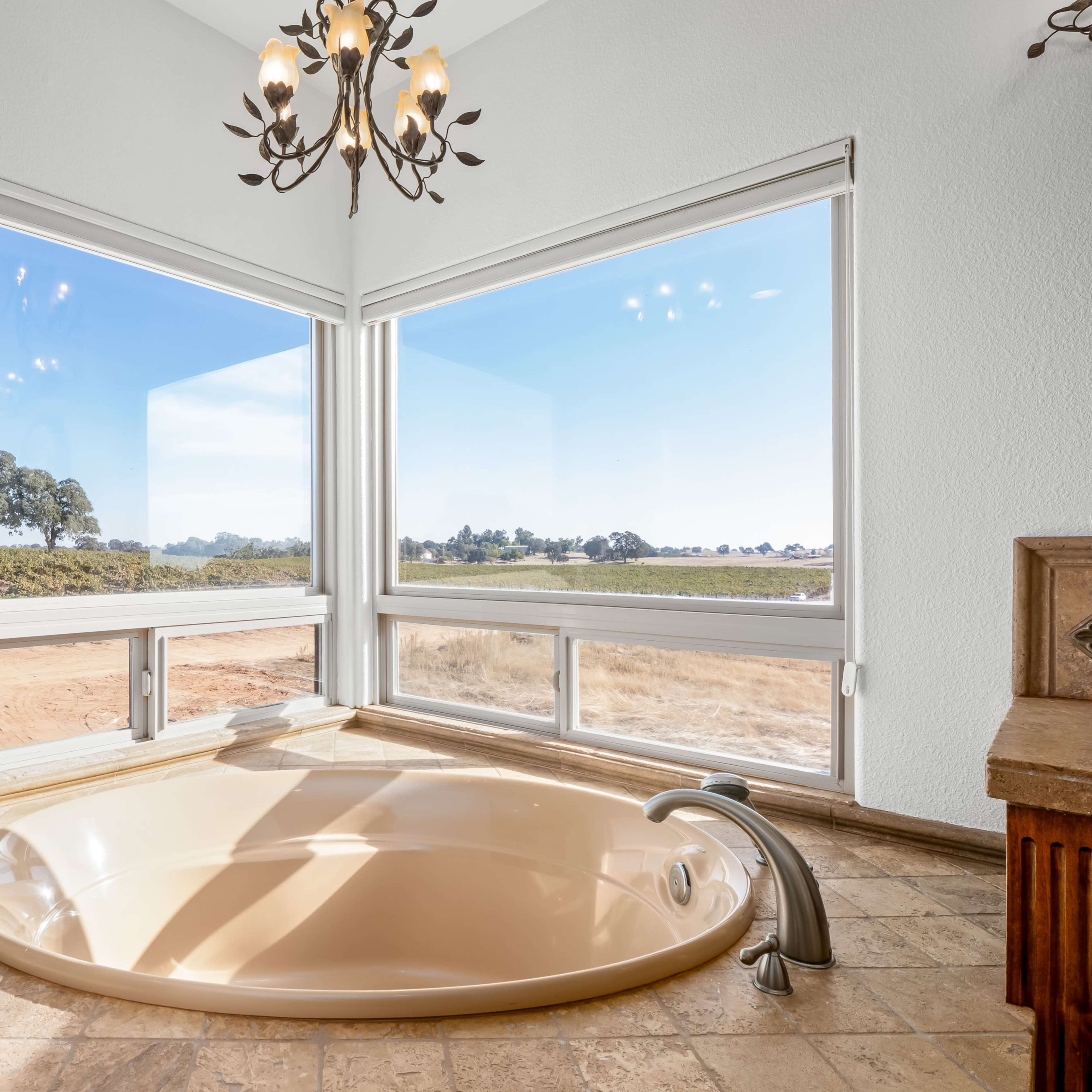 A large circular bathtub is situated in a room with expansive windows offering a view of a landscape with trees and fields.