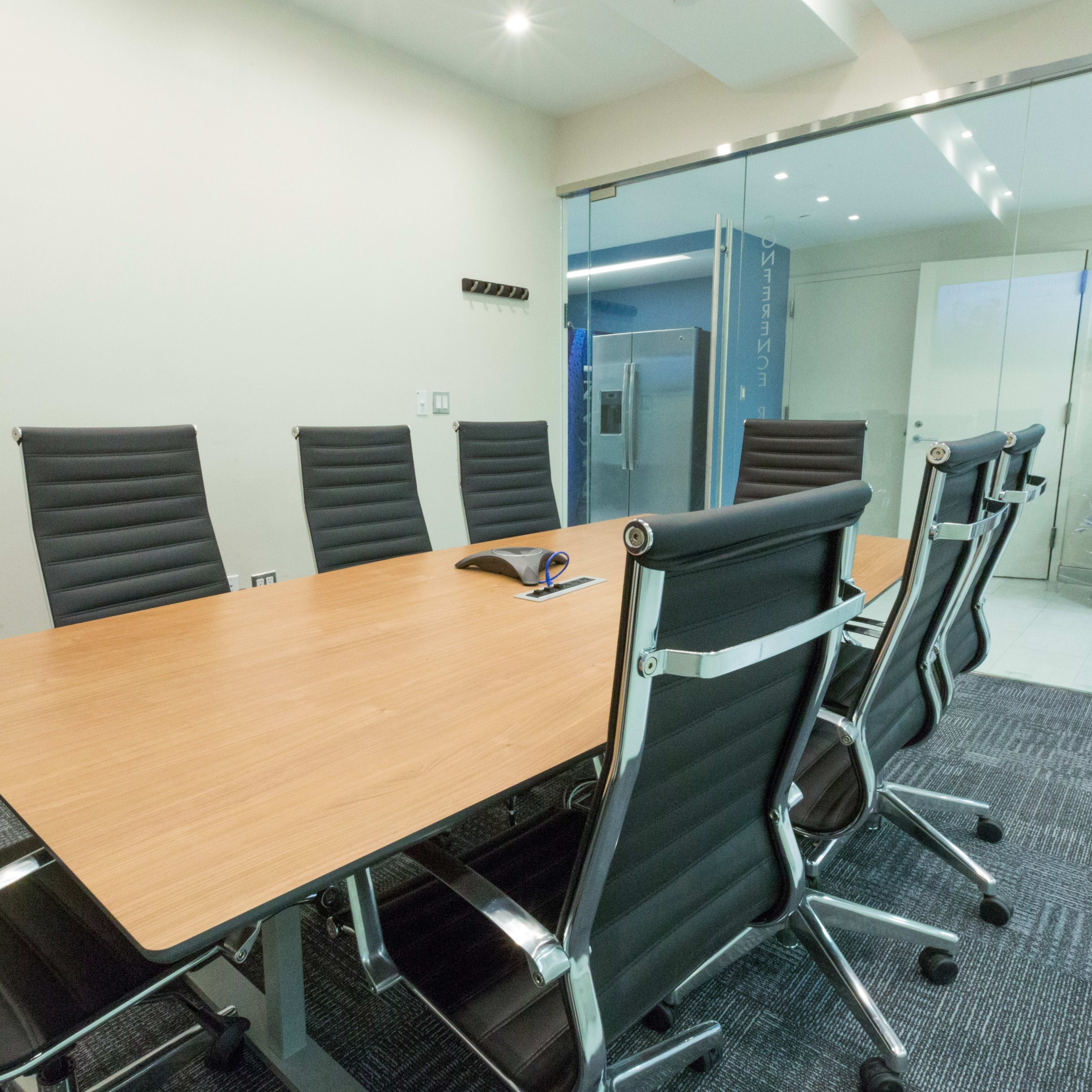 A modern conference room features a large wooden table surrounded by eight black office chairs.