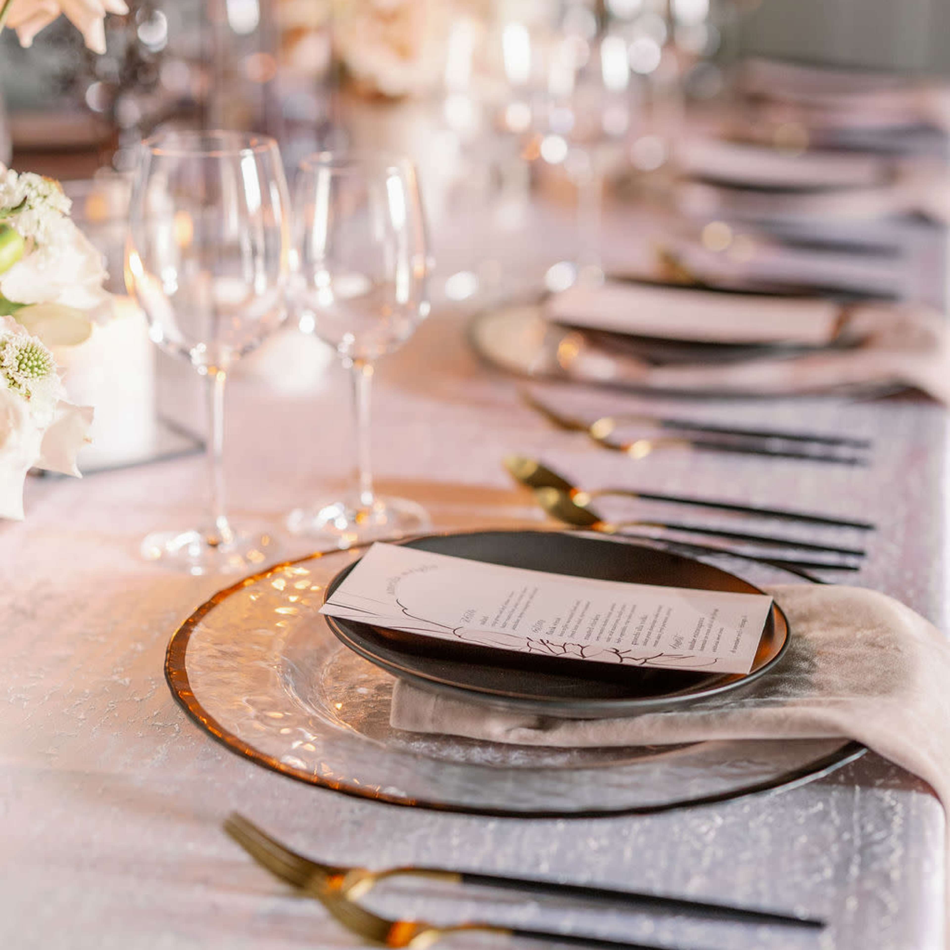 A elegantly set dining table adorned with floral arrangements, glassware, and neatly arranged plates, illuminated by candles.