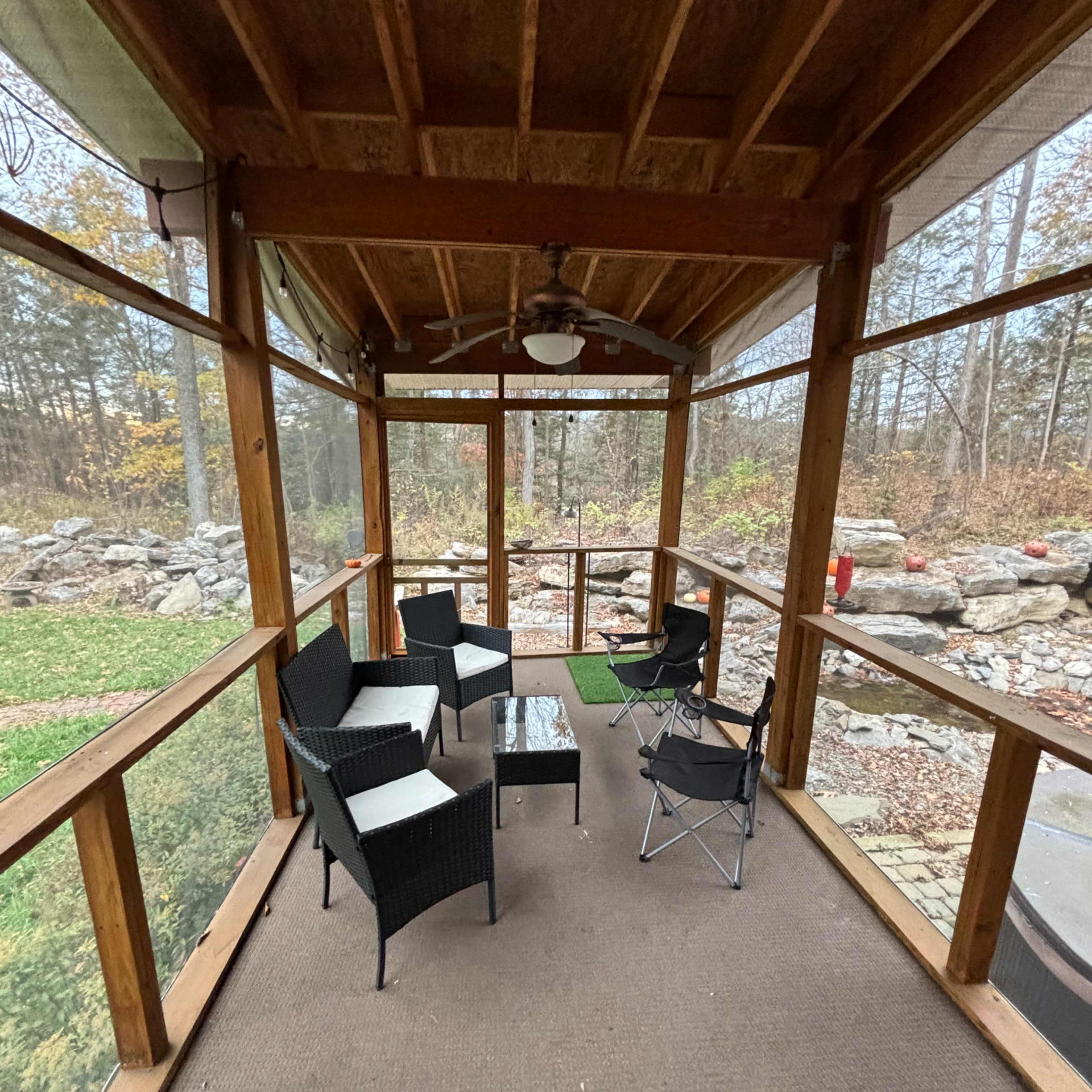 A screened-in porch with several chairs and a small table overlooking a garden area.