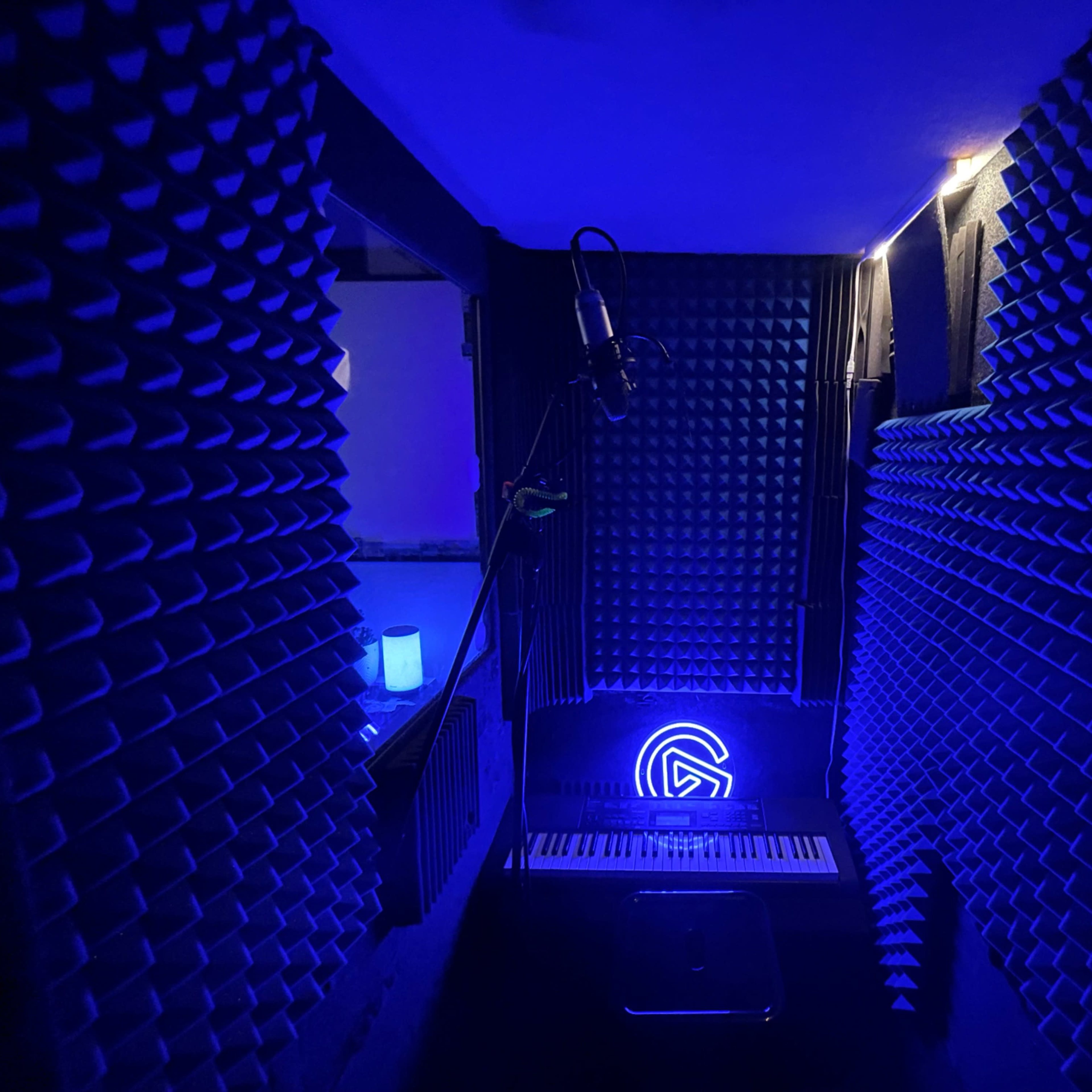 A soundproof recording studio with foam sound panels, a microphone on a stand, and blue ambient lighting.