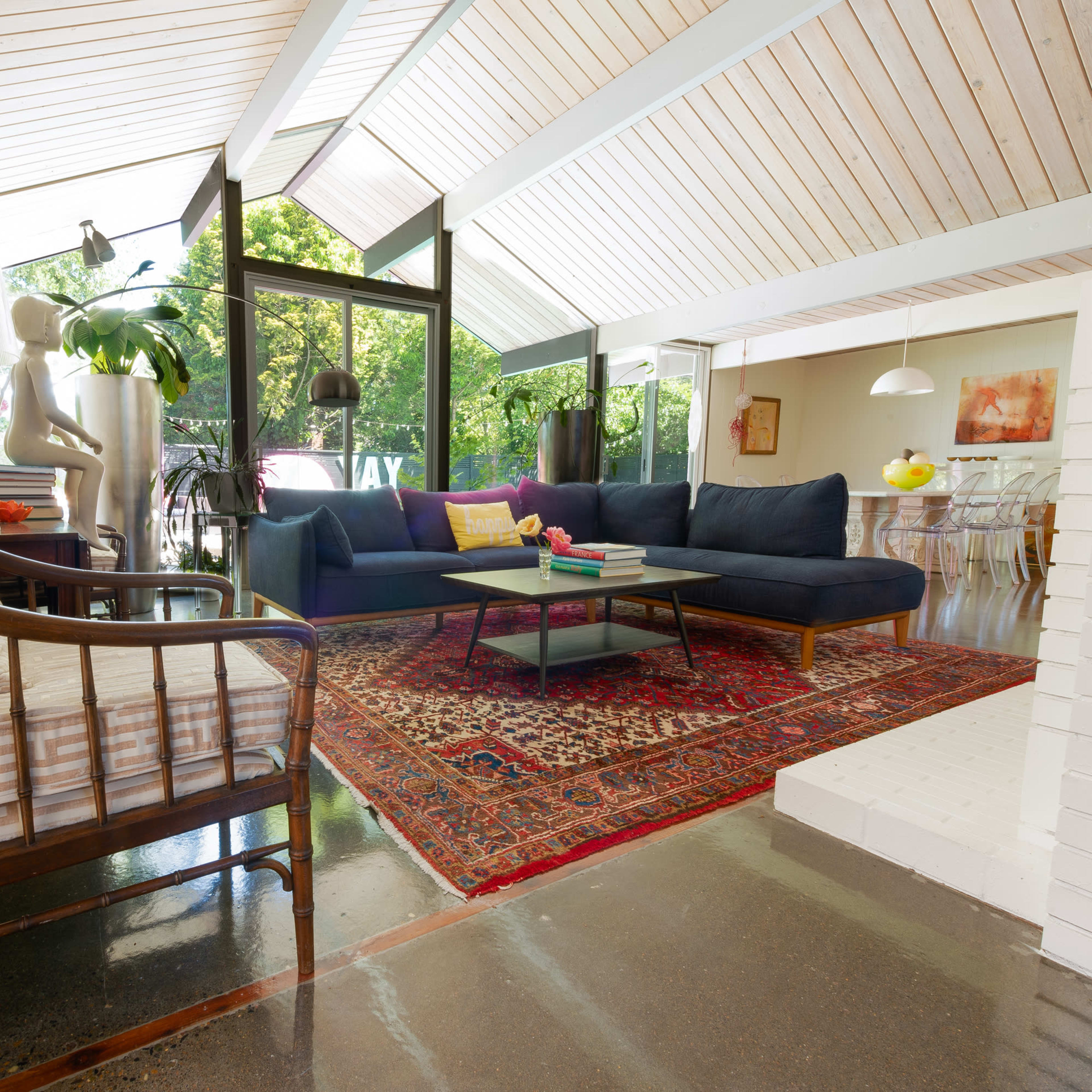 A modern living room features a dark sectional sofa, a patterned rug, and large windows that allow natural light to illuminate the space.