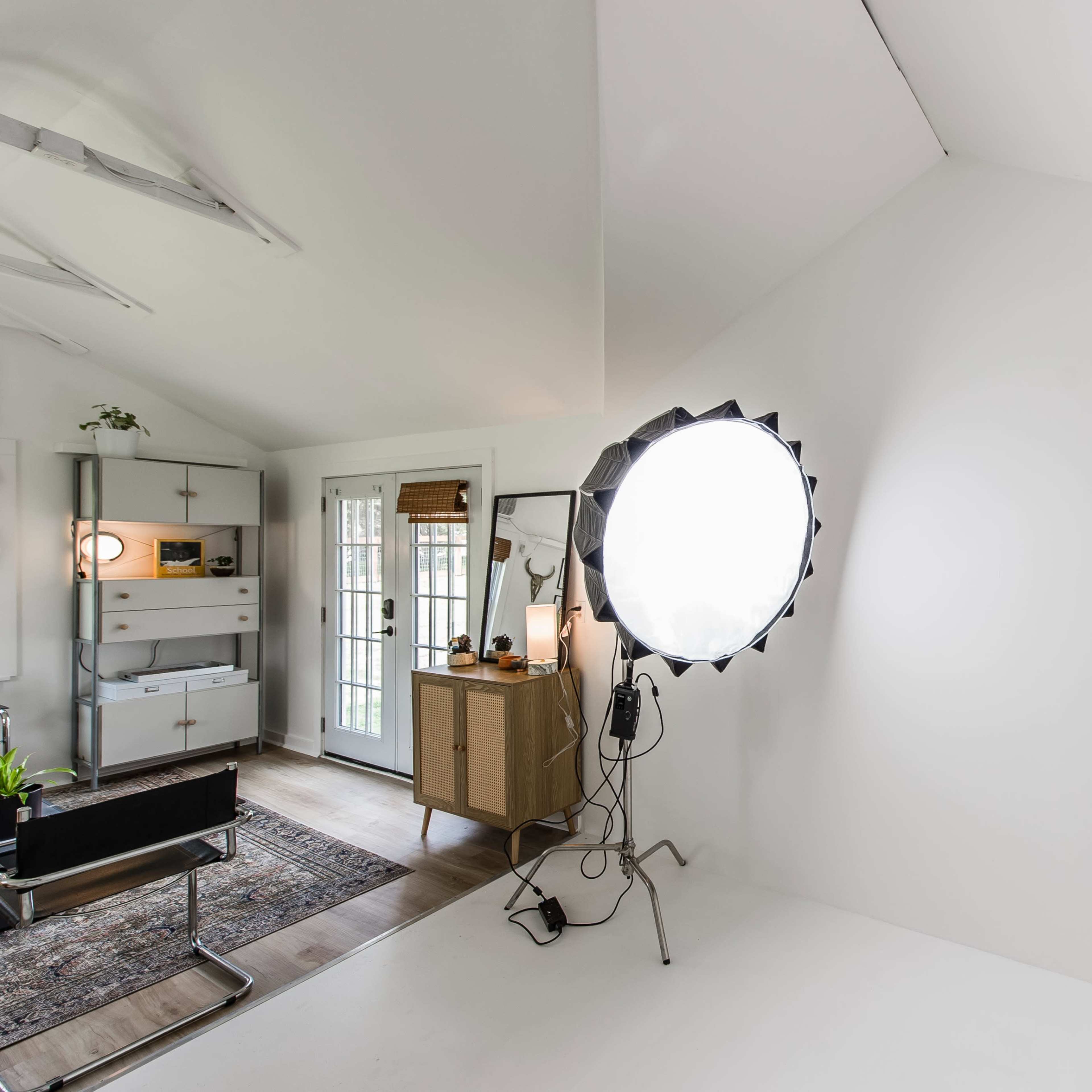 A bright, minimalistic studio space featuring a circular softbox light and a neutral-colored wall.