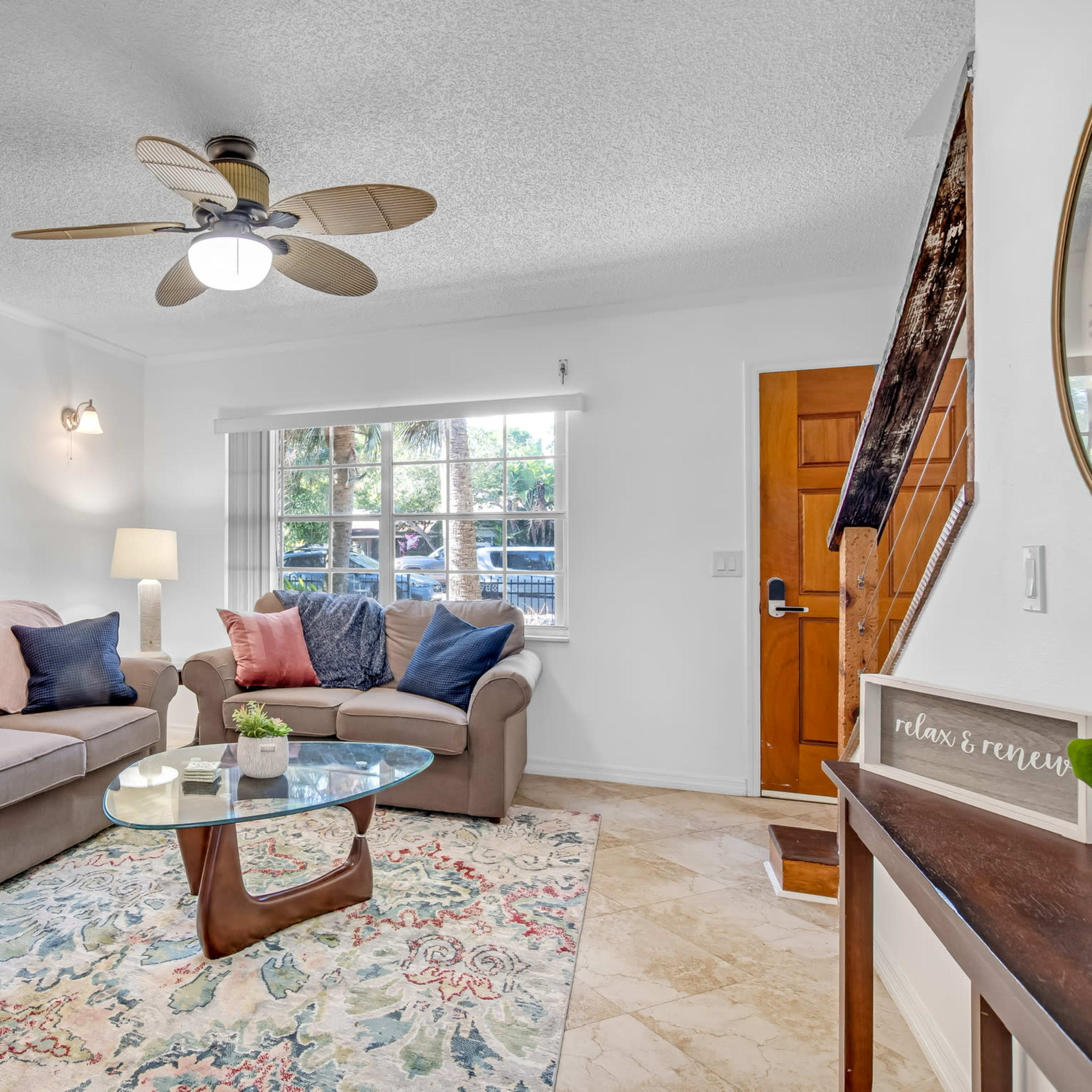 A cozy living room features a sofa, a glass coffee table, and a large window with a view of the outdoors.