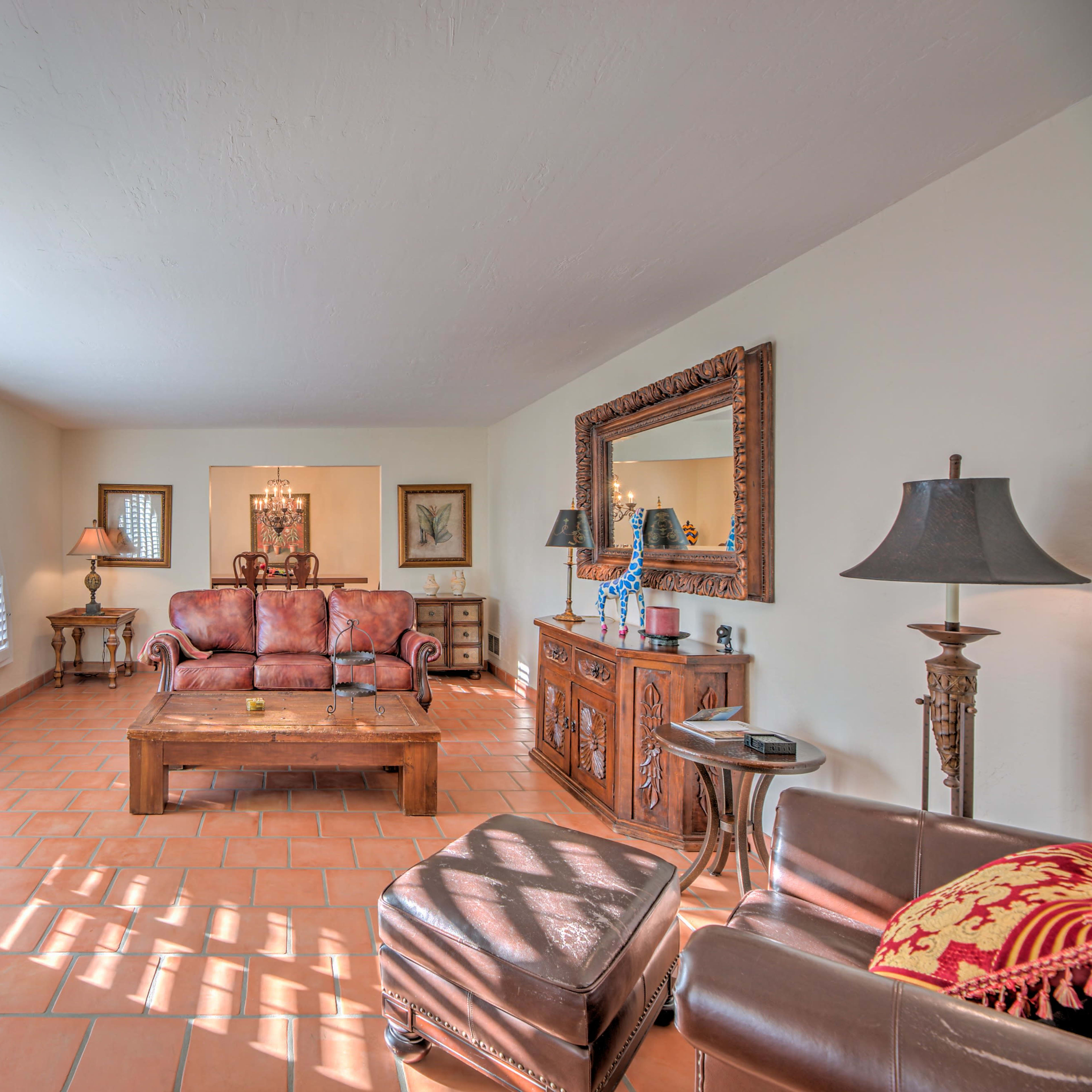 A spacious living room with arched windows, terracotta tile flooring, and a mix of wooden furniture.