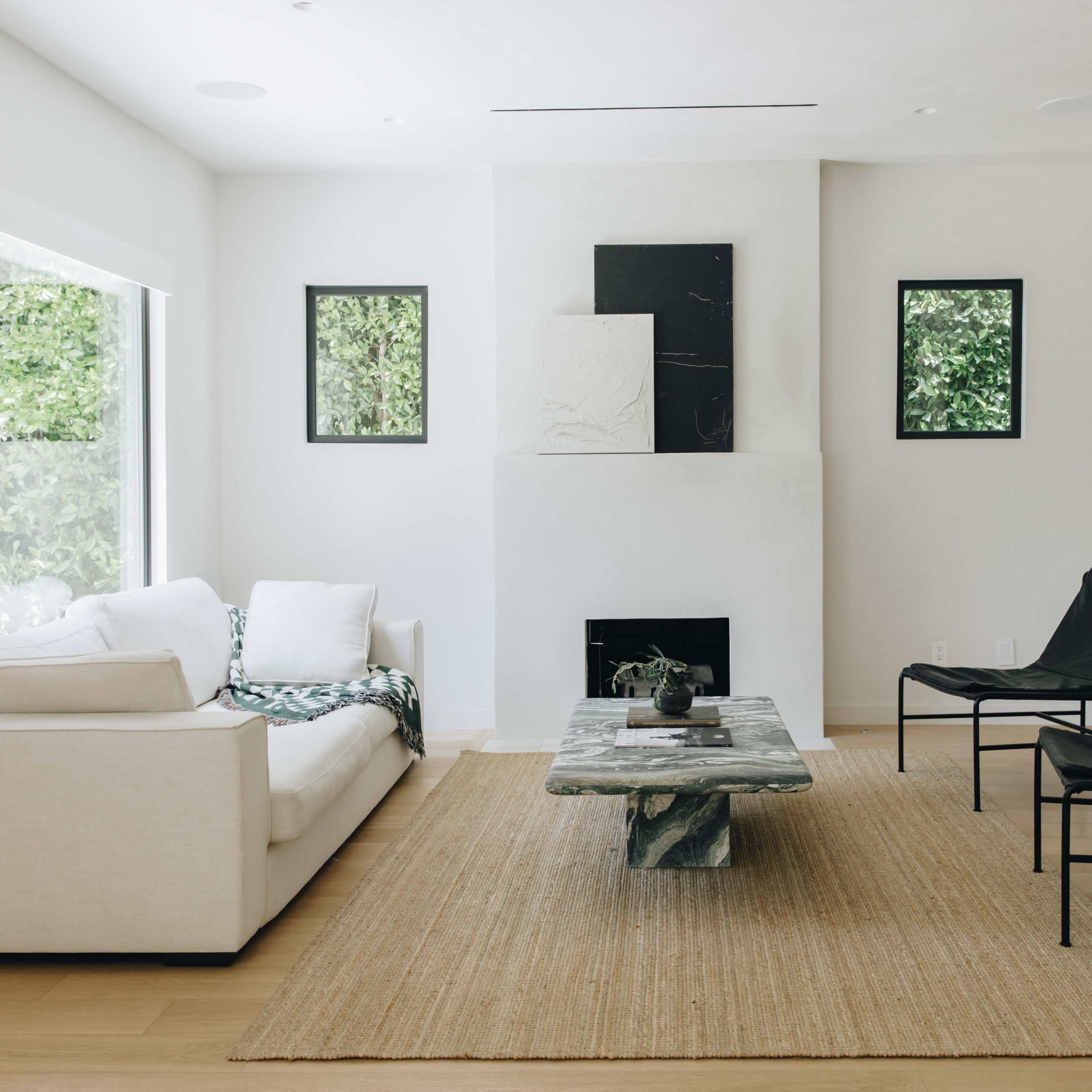 A minimalist living room features a white sofa, a black coffee table, two black chairs, and artwork on the walls.
