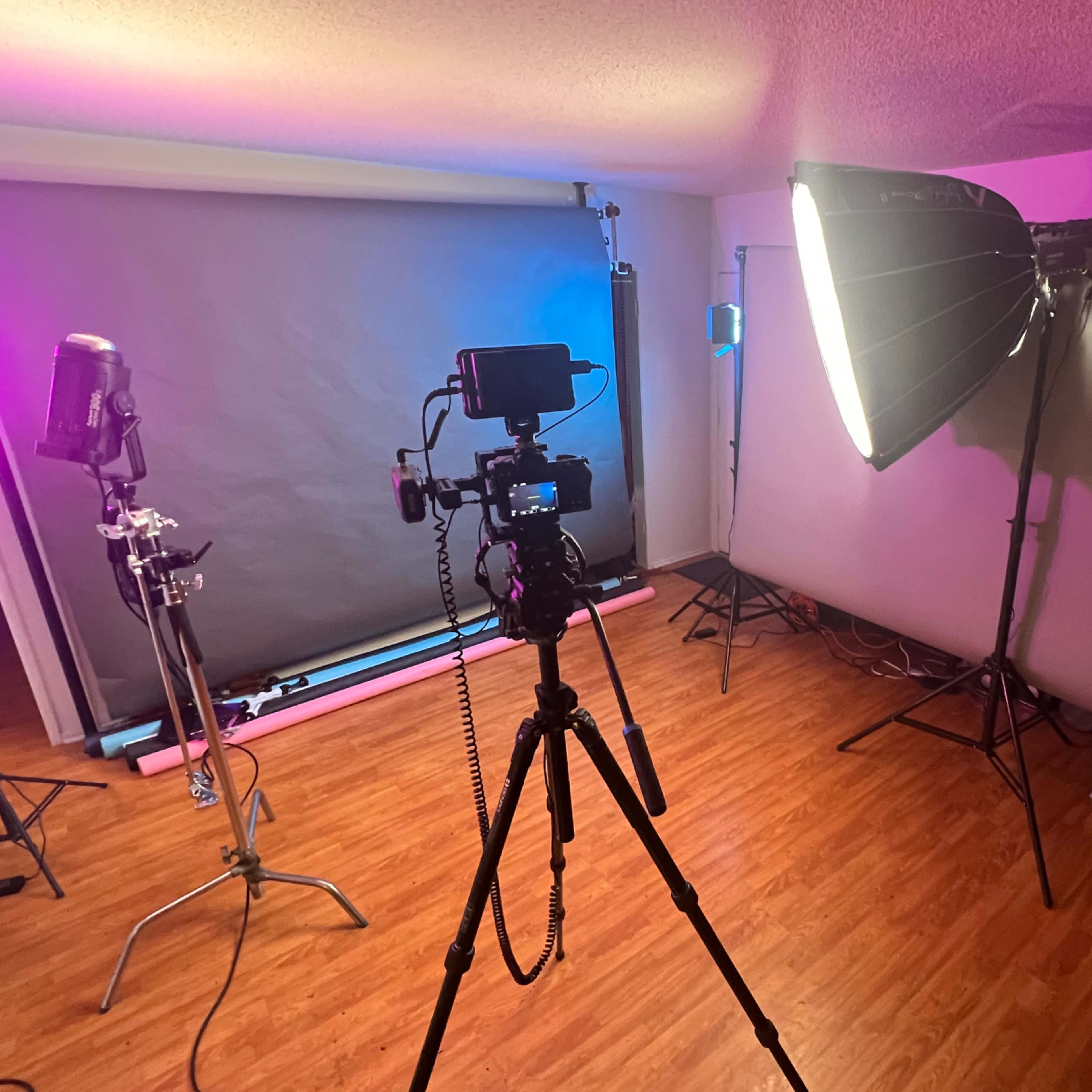 A photography studio setup with a camera on a tripod, light sources, and backdrop supports.