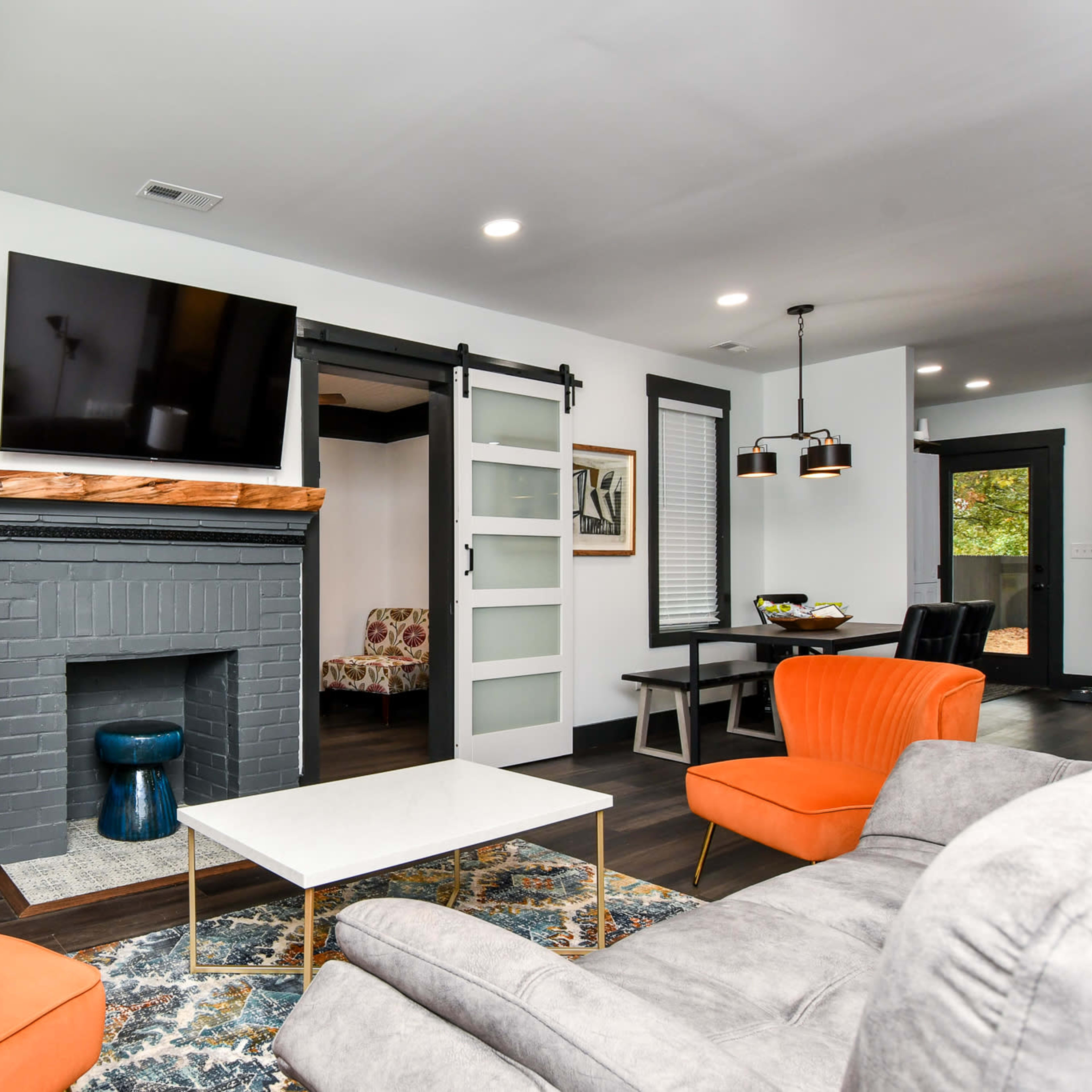 The living room features orange armchairs, a gray brick fireplace, a wall-mounted television, and a sliding glass door leading to another room.